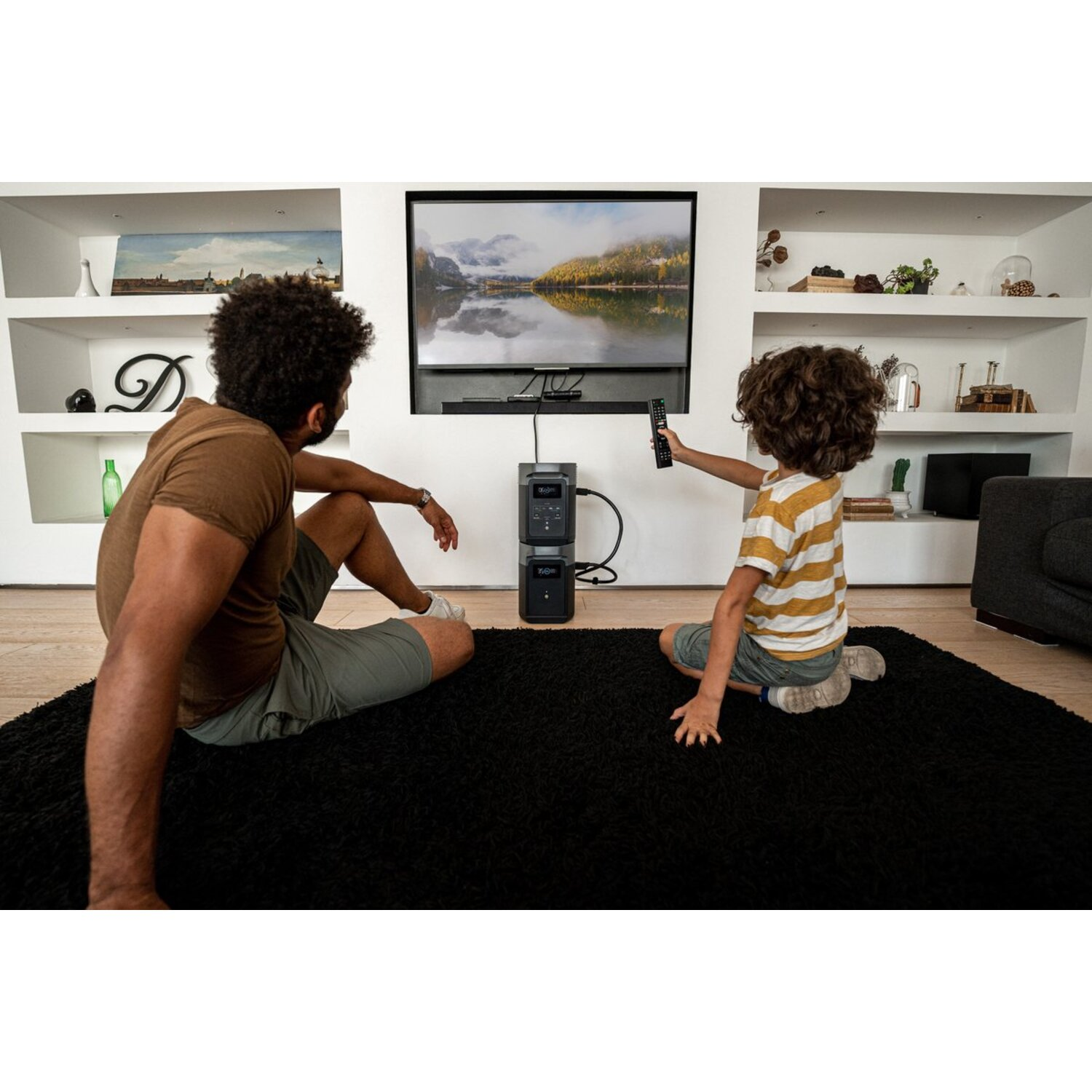 A man and a child are sitting on a rug in front of a TV, the child is holding a remote.
