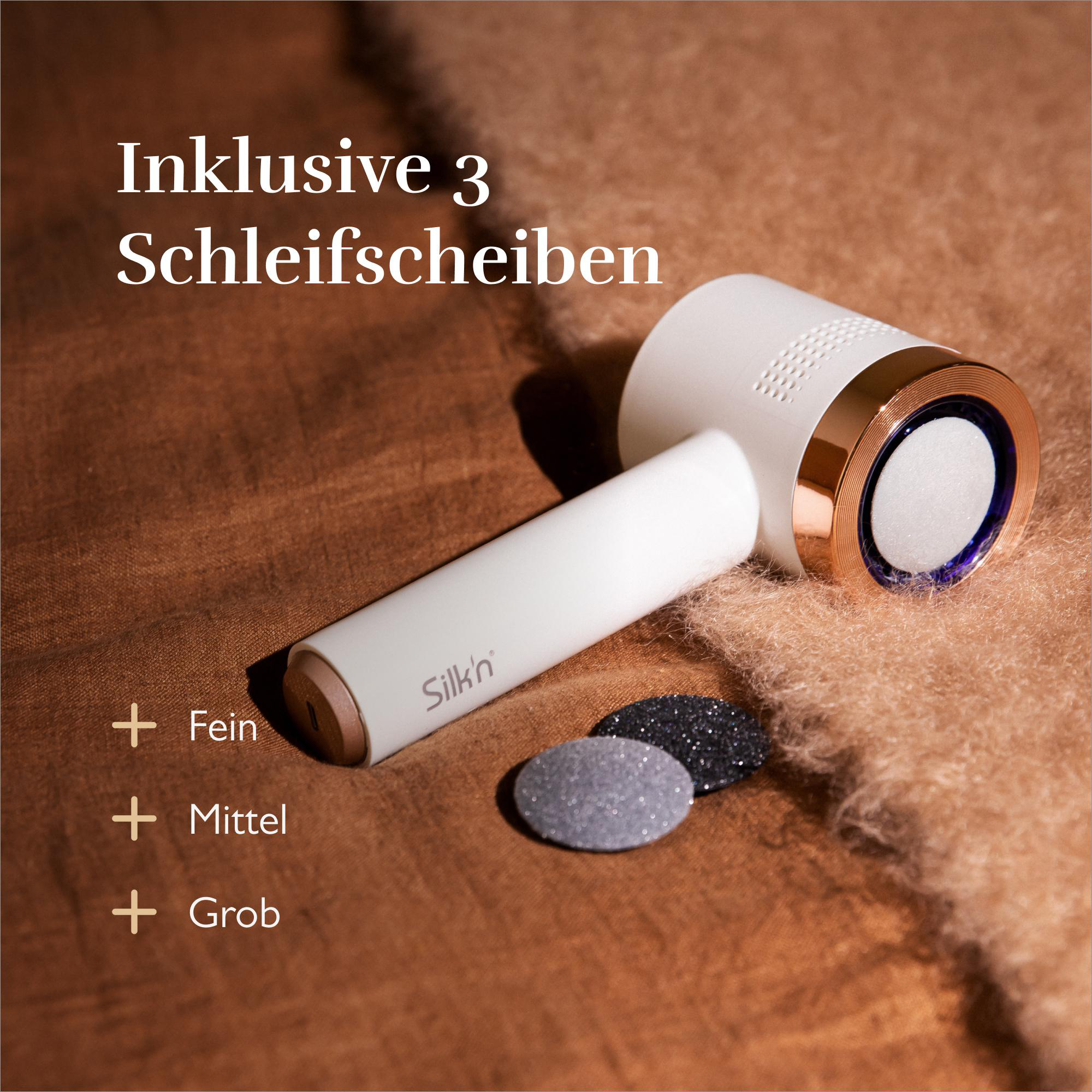Weißes Fußpflegegerät mit roségoldenen Akzenten und drei Schleifaufsätzen. Brauner Hintergrund.