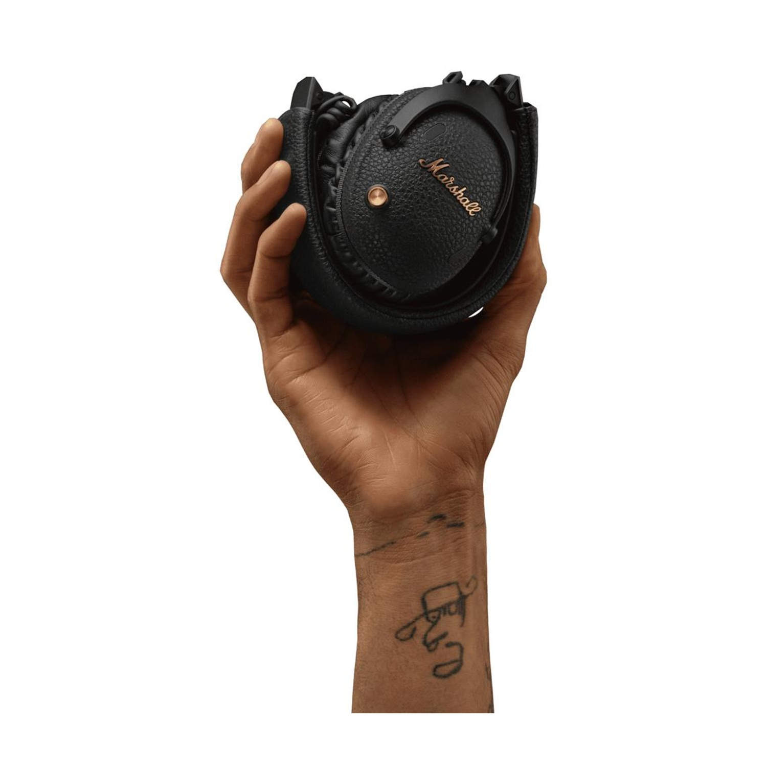 Cuffie nere tenute in mano. Tatuaggio sul braccio. Sfondo bianco.