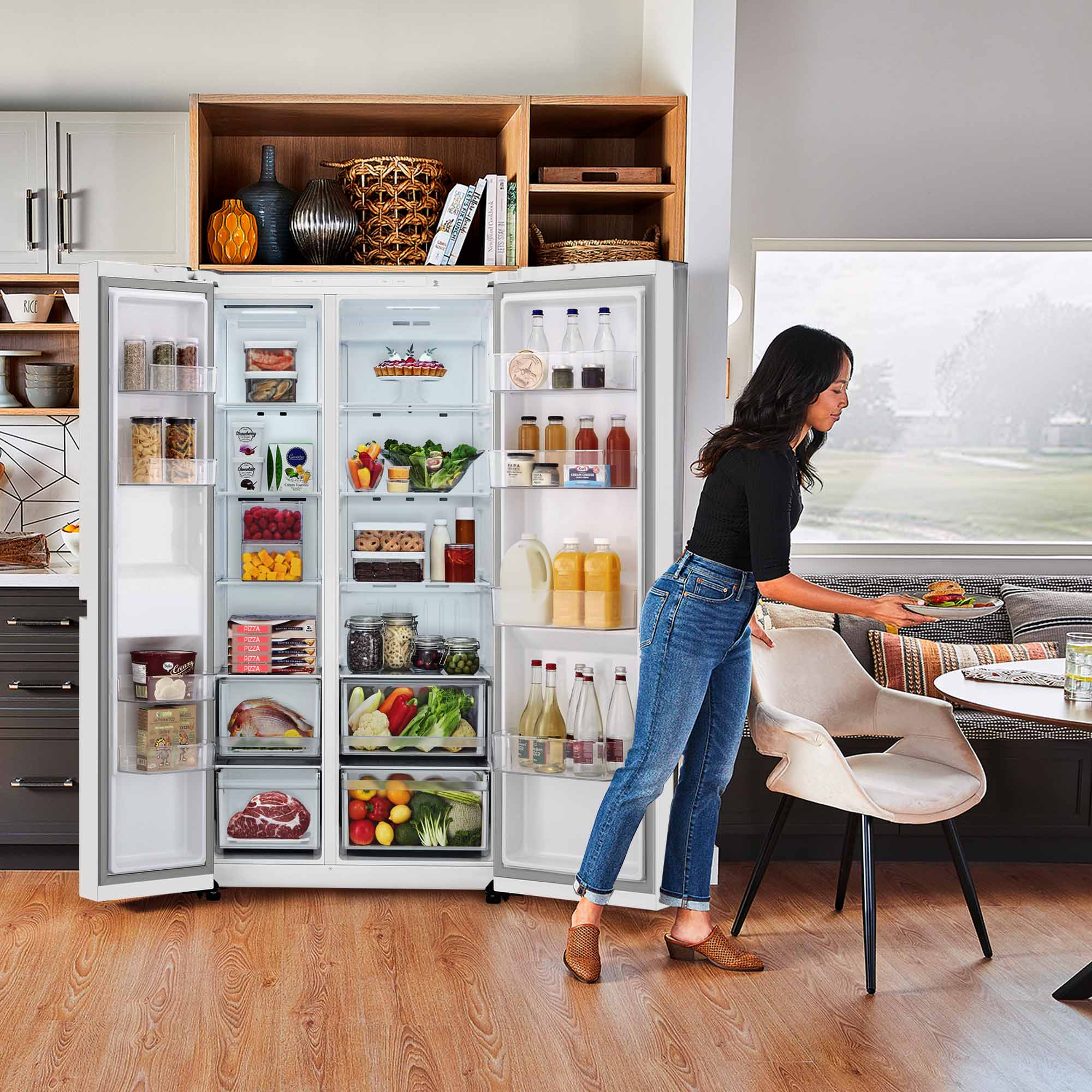 Una mujer metiendo la mano en un refrigerador lleno de comida, con una mesa de comedor al fondo.