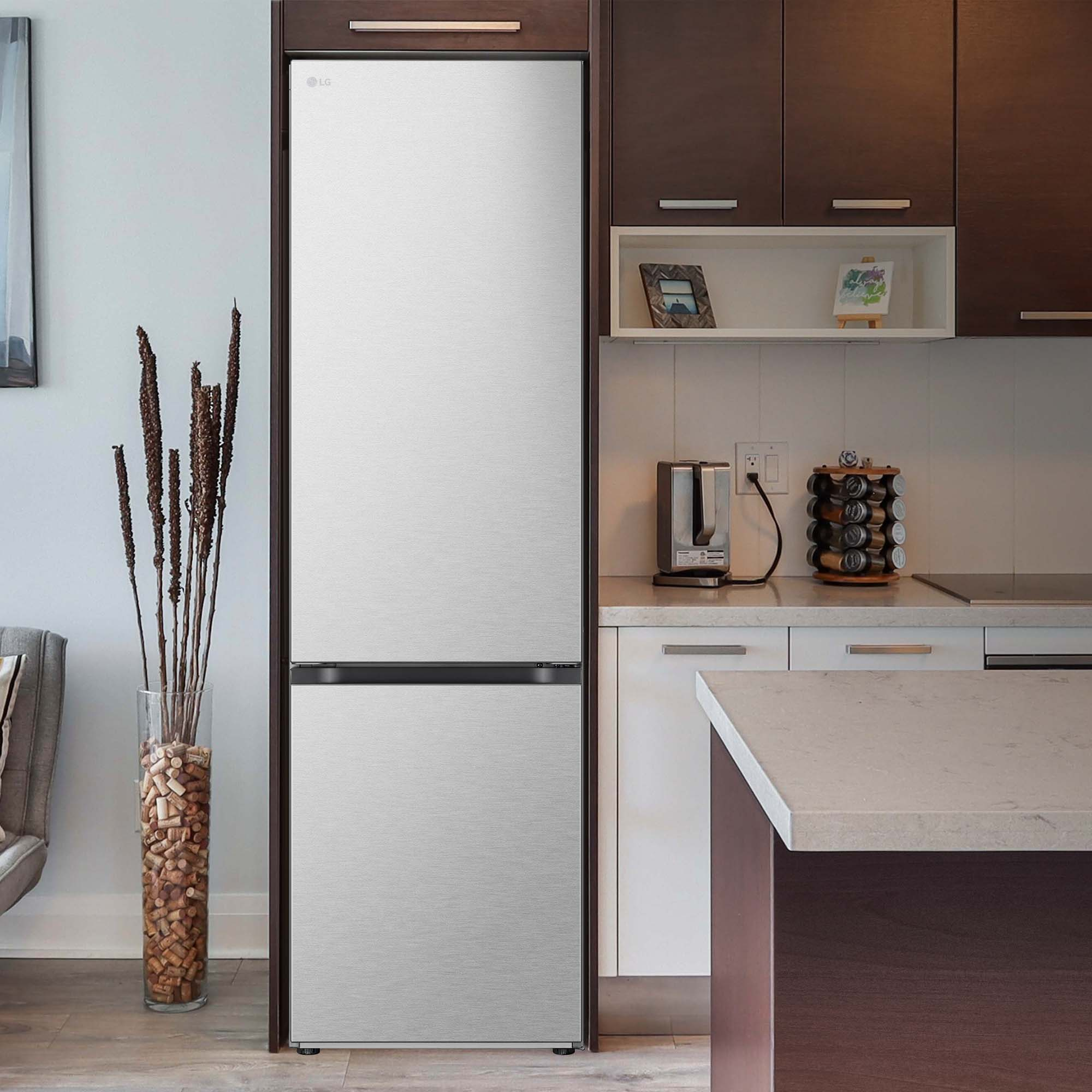 Un refrigerador en una cocina con gabinetes de madera oscura. Un jarrón con palos está a la izquierda. Una encimera de color claro.
