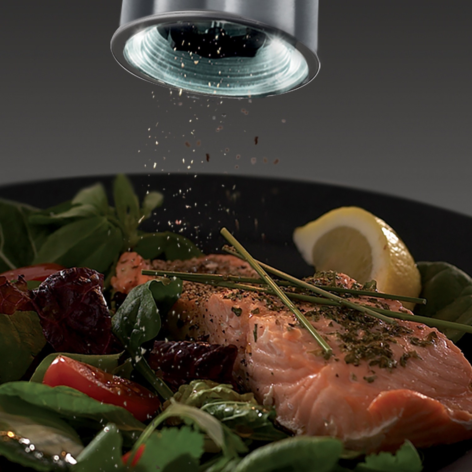 Salmone con verdure e un macina spezie che spruzza erbe aromatiche sul cibo.