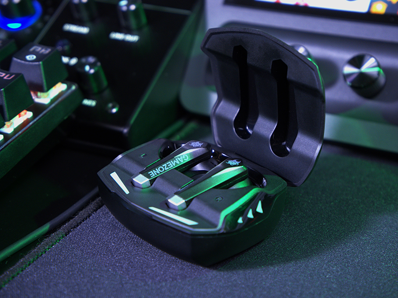 Słuchawki do gier w otwartym etui ładującym, czarno-zielony design, na biurku.