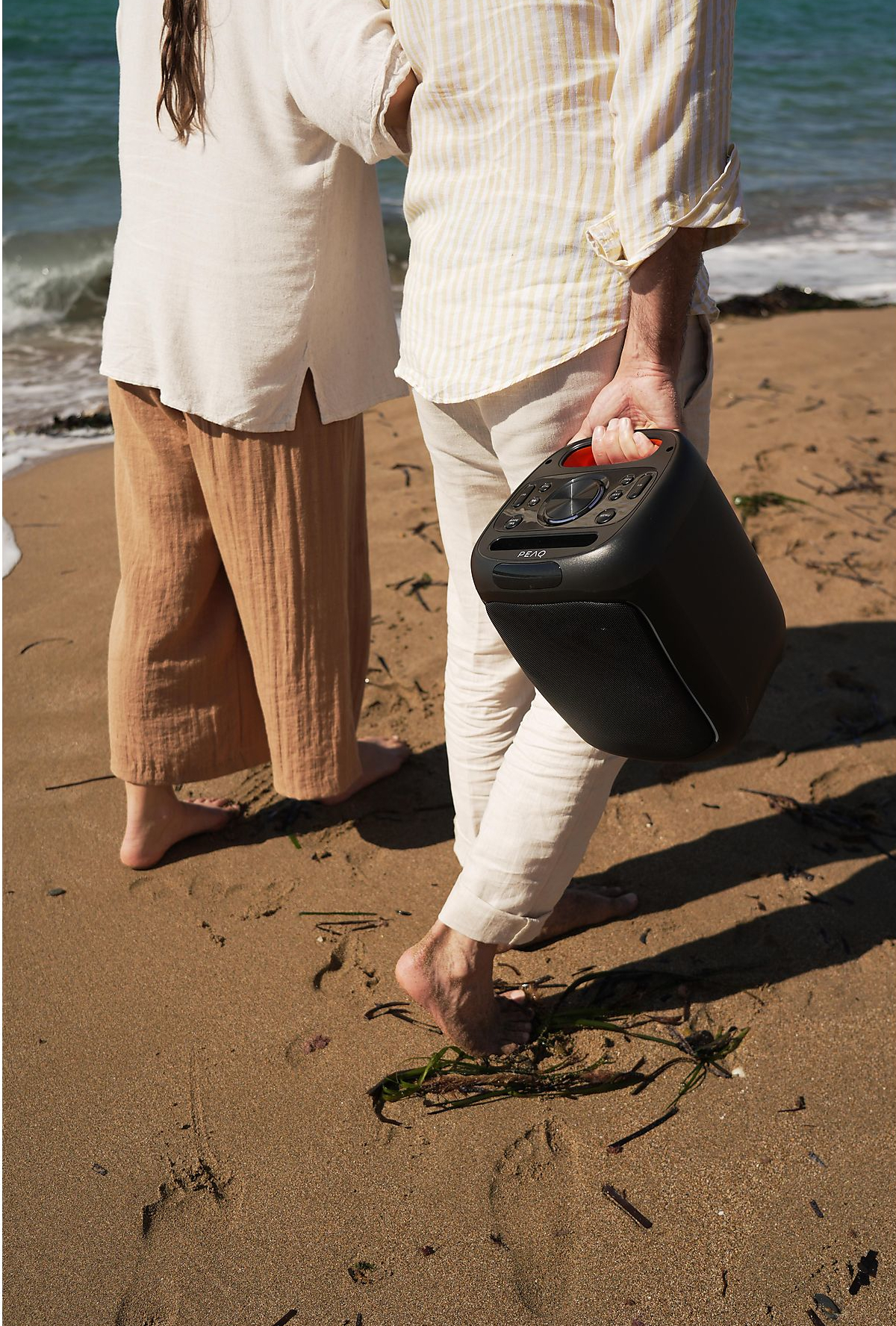 Para na plaży z czarnym głośnikiem, piaskiem i błękitnym niebem.