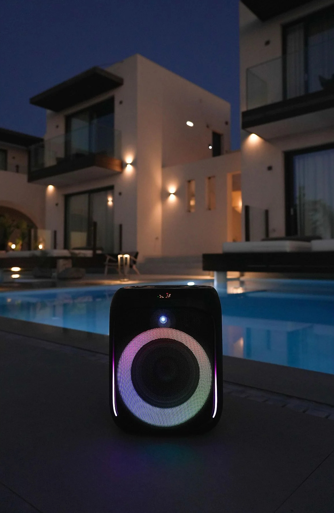 Czarny głośnik przy basenie w nocy, z kolorowo podświetlanym głośnikiem.