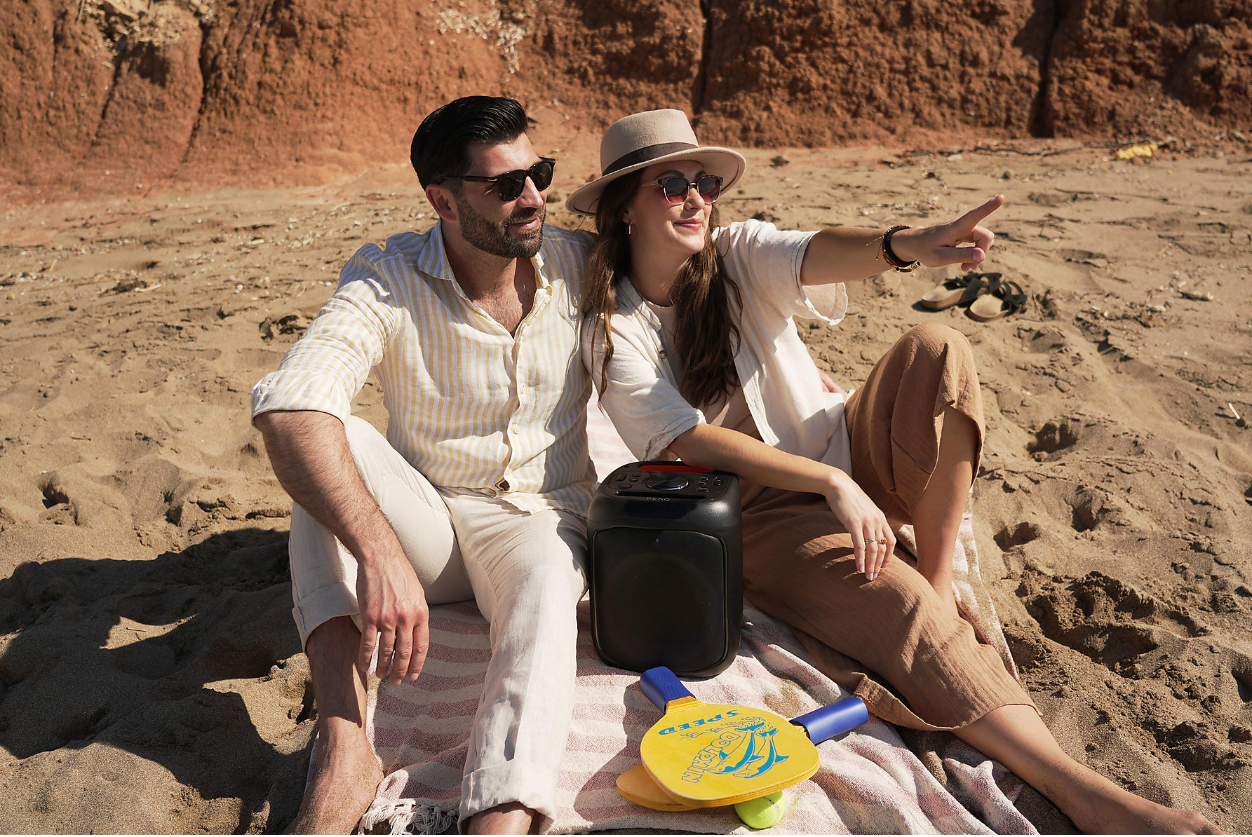 Para na plaży, mężczyzna wskazuje, z głośnikiem i wiosłami.