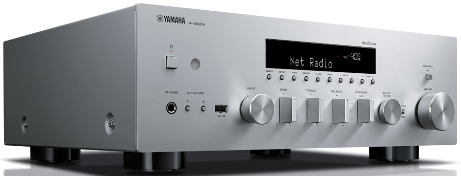 Srebrny odbiornik stereo Yamaha z przyciskami i wyświetlaczem pokazującym 'Net Radio'. Jest na stole.