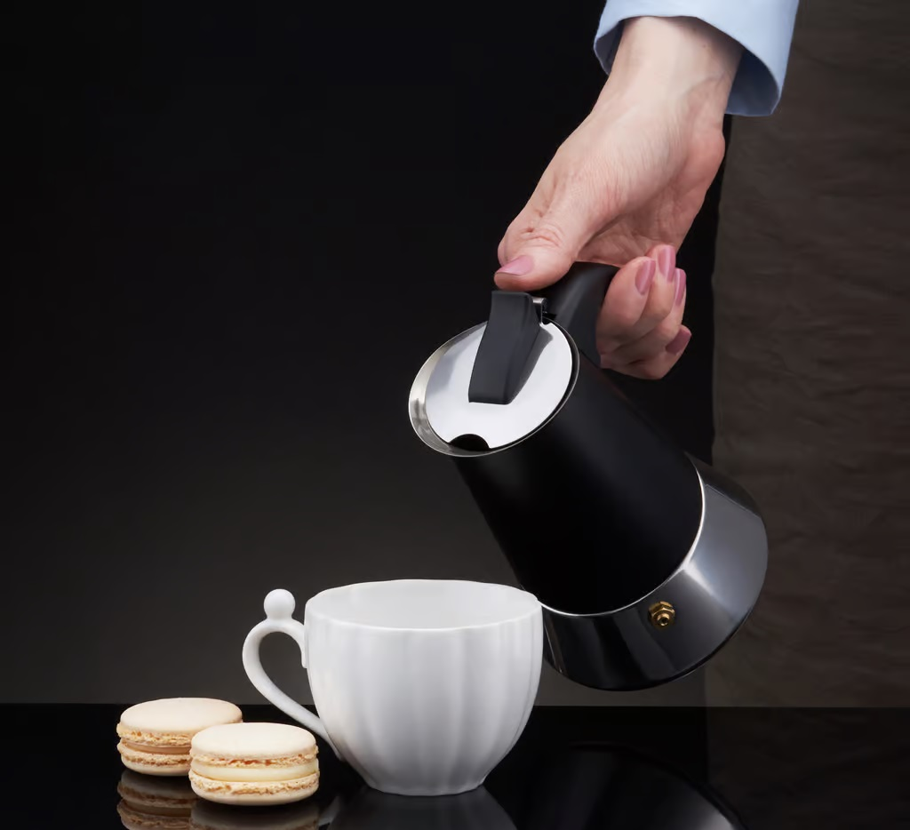 Osoba nalewa z czarnego i srebrnego dzbanka do kawy do białego kubka.