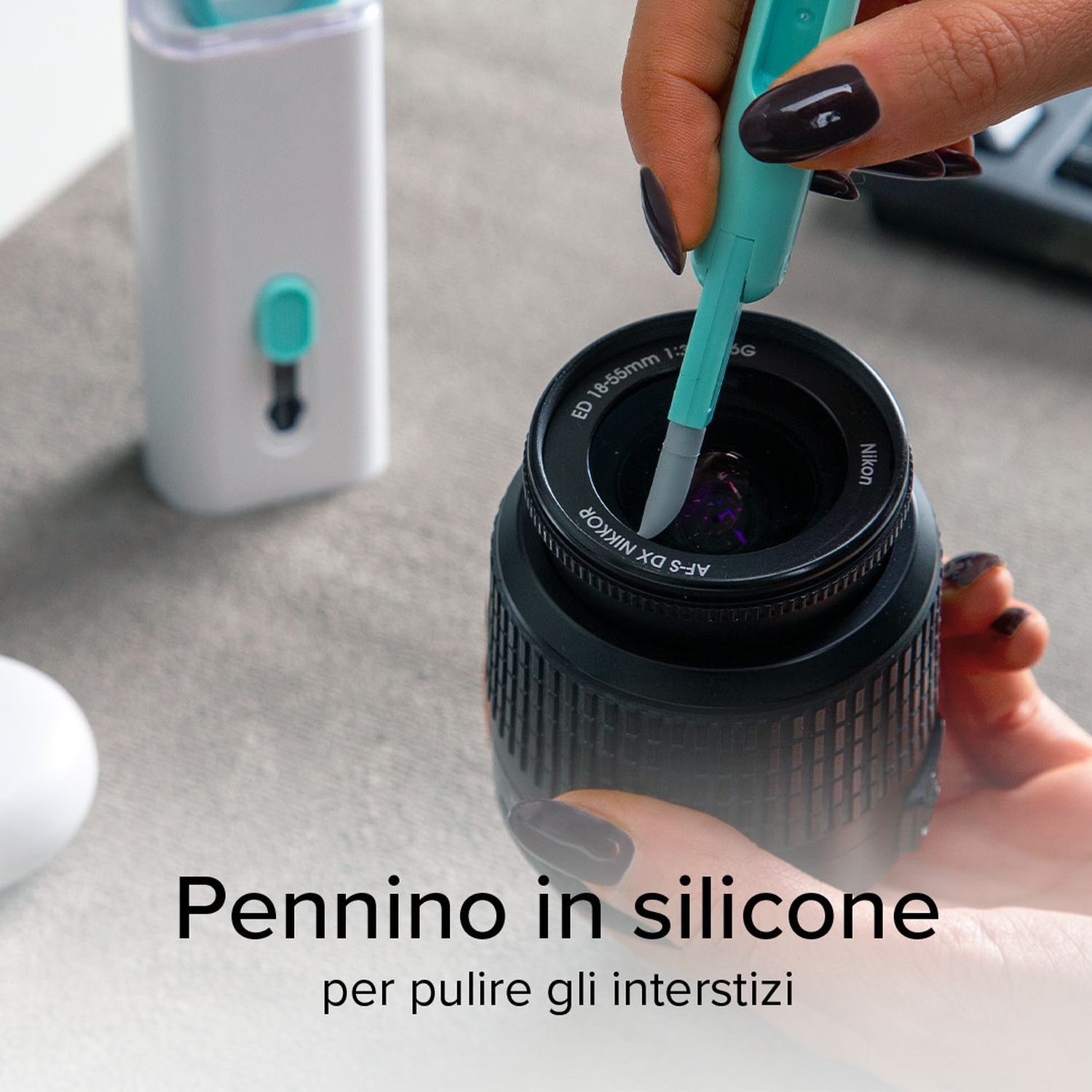 Mani che puliscono un obiettivo della fotocamera con una spazzola in silicone. Strumento di pulizia bianco sullo sfondo.