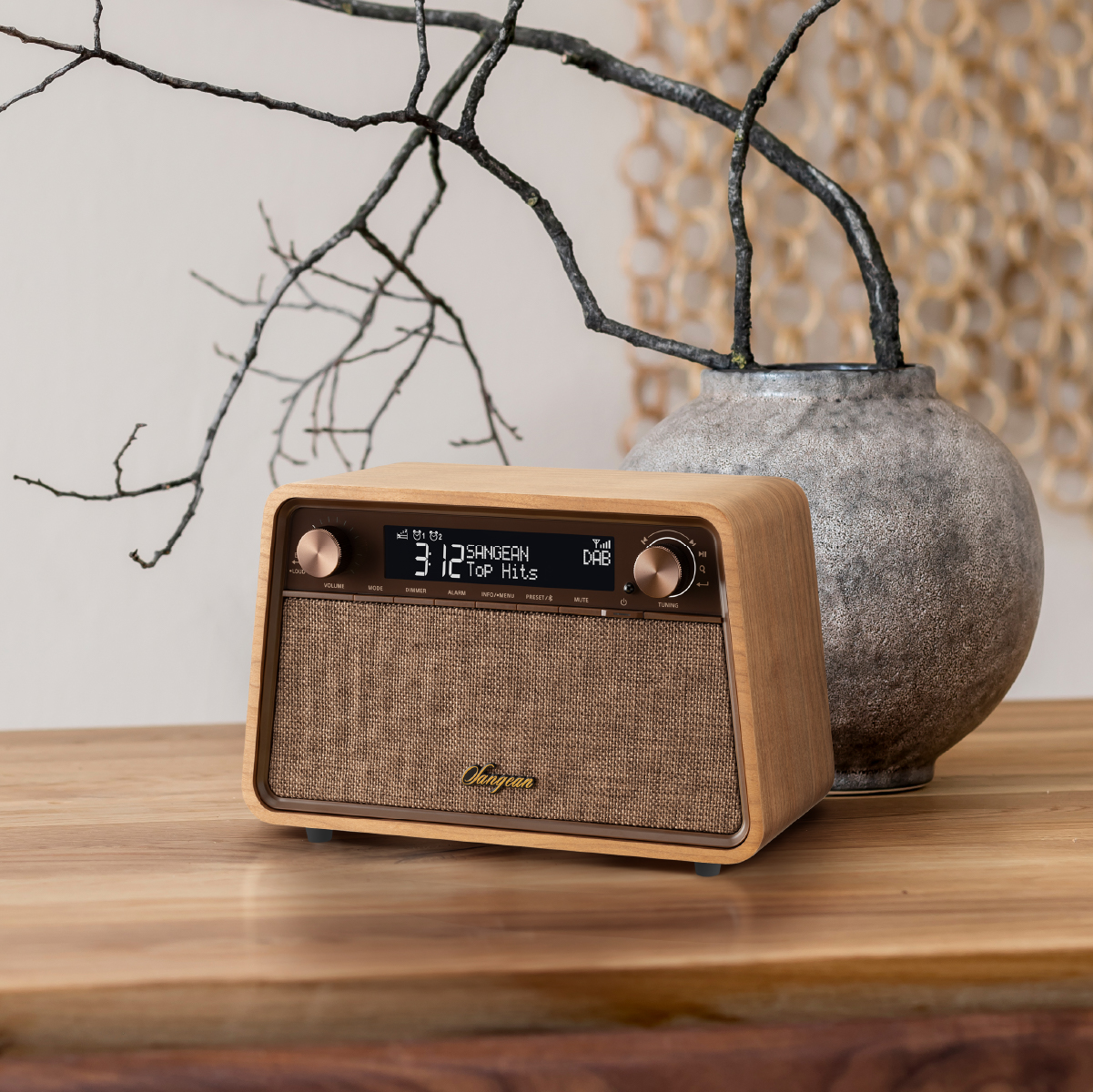 Holzradio auf einem Holztisch. Eine Vase mit Zweigen und ein gewebter Hintergrund. Heller Hintergrund.