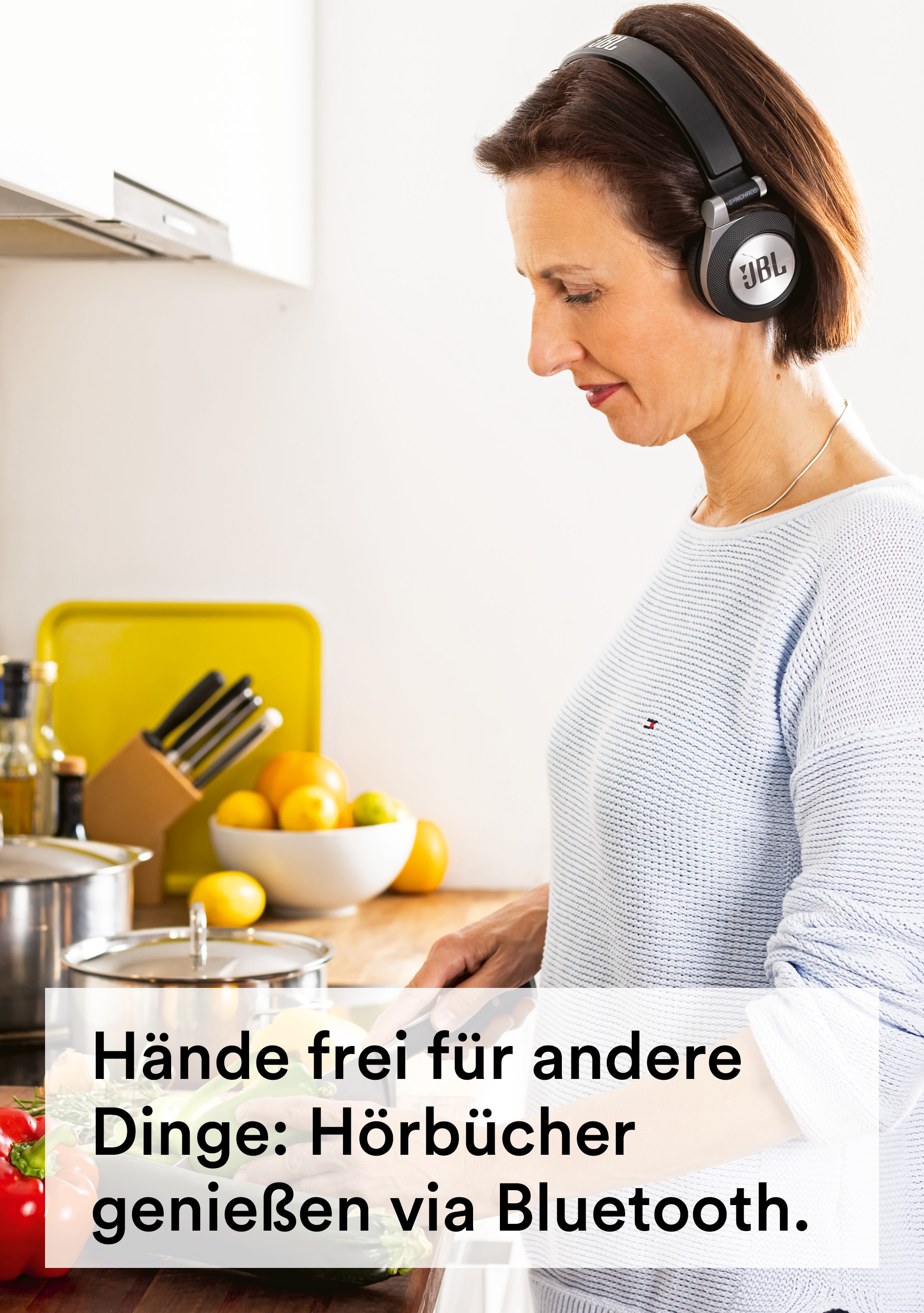 Eine Frau in einer Küche mit Kopfhörern, hält ein Messer, bereitet Essen zu, in der Nähe einer Schüssel mit Zitronen.