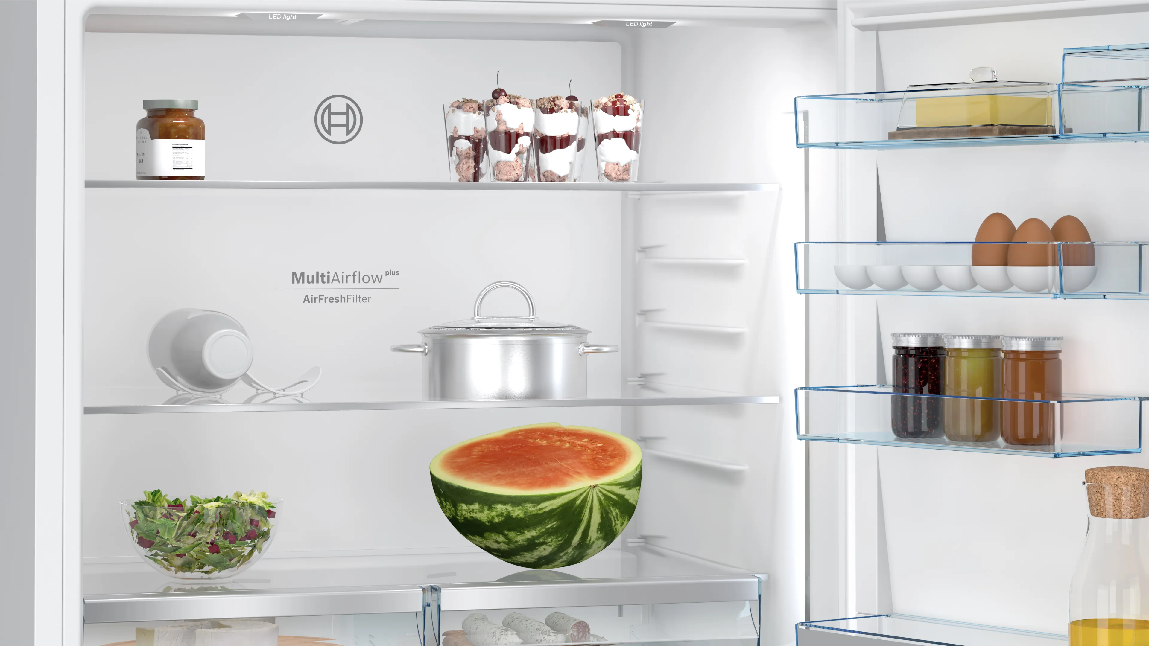 Bir buzdolabının içi. Karpuz, salata, tatlılar, yumurta ve kavanoz yiyecekler içerir.