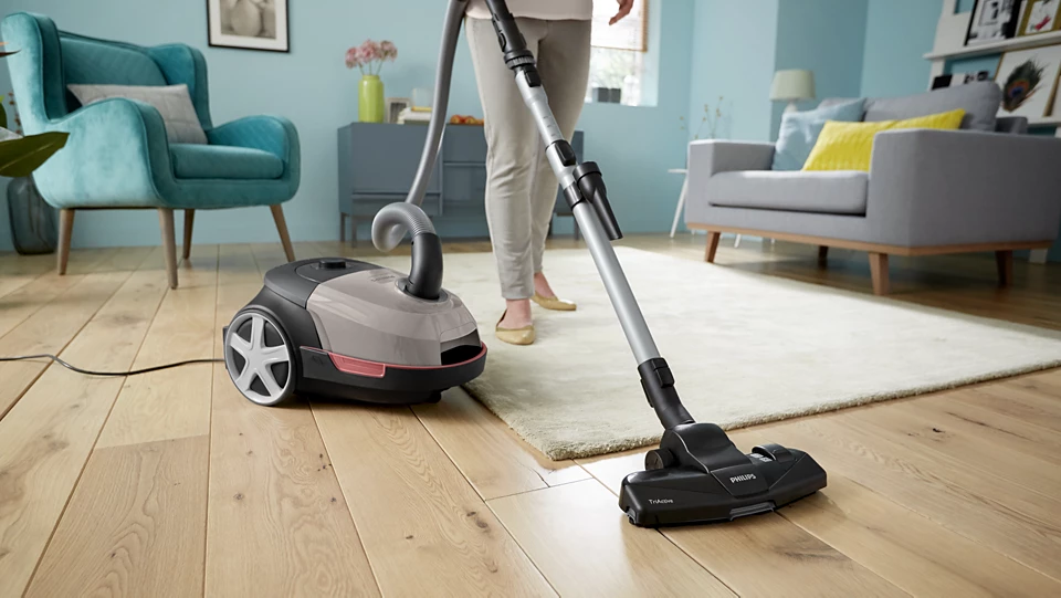 Személy porszívózik egy fapadlót egy Philips porszívóval a nappaliban.