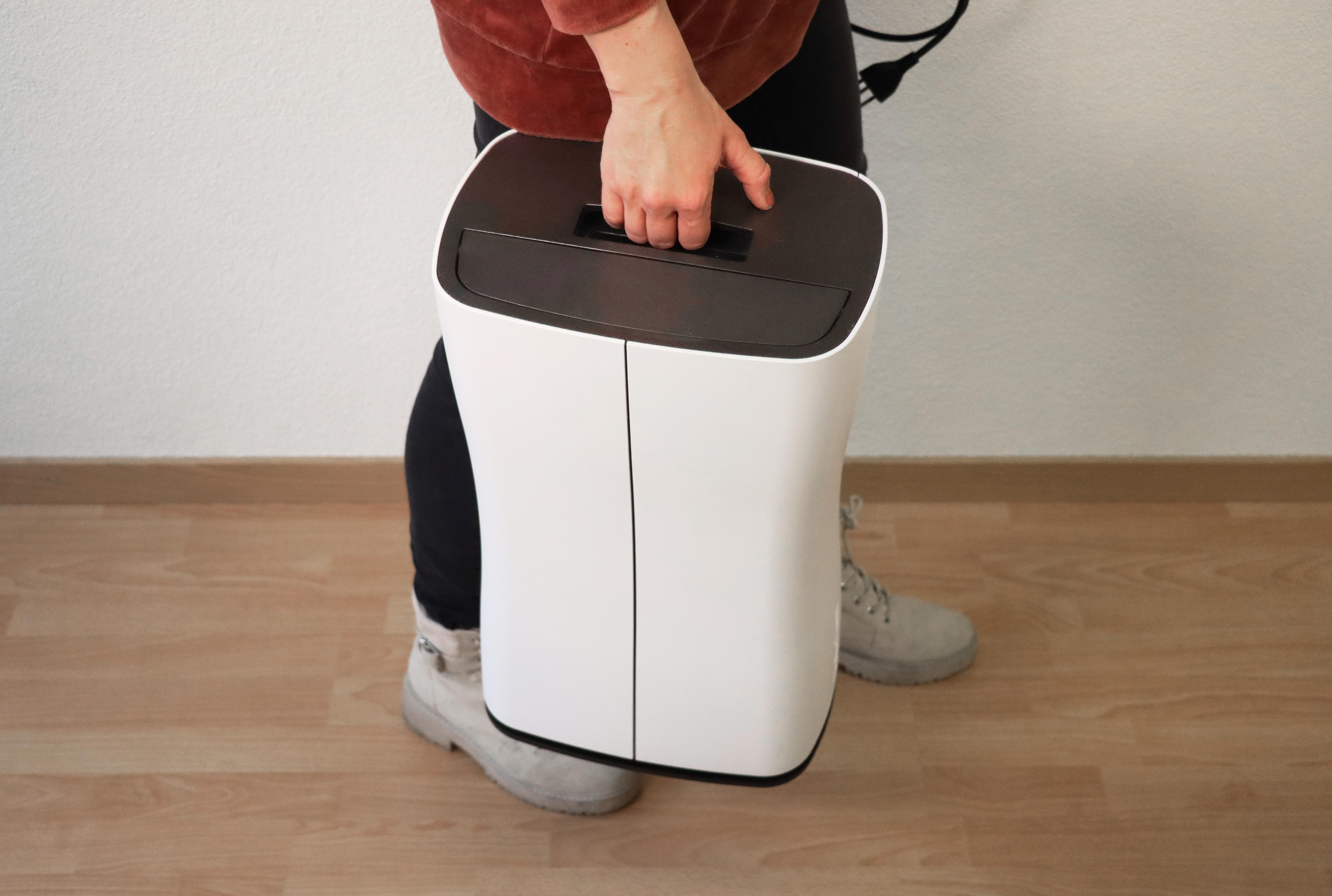 Person hält einen weiß-schwarzen Aktenvernichter. Sie stehen auf einem Holzboden.