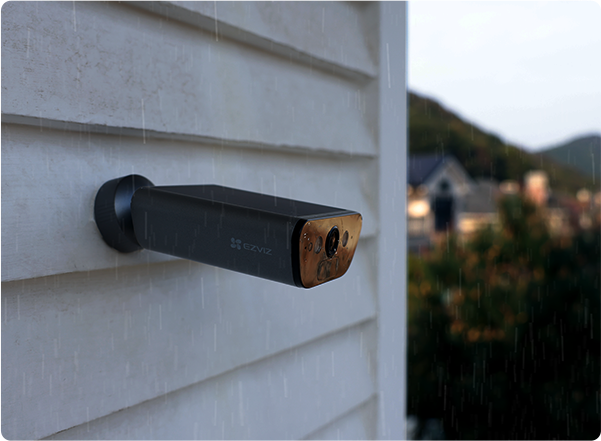 Kültéri biztonsági kamera fehér fa falra szerelve.