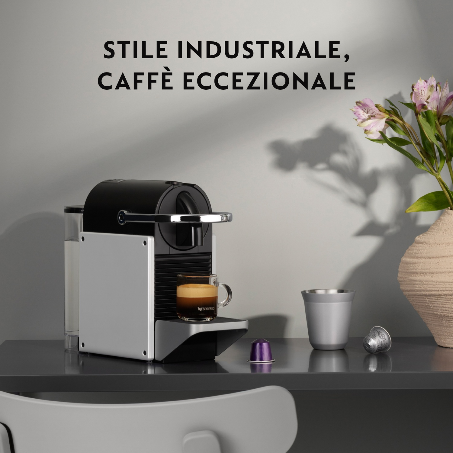 Macchina Nespresso con una tazza di caffè su un tavolo, con una capsula e un vaso.