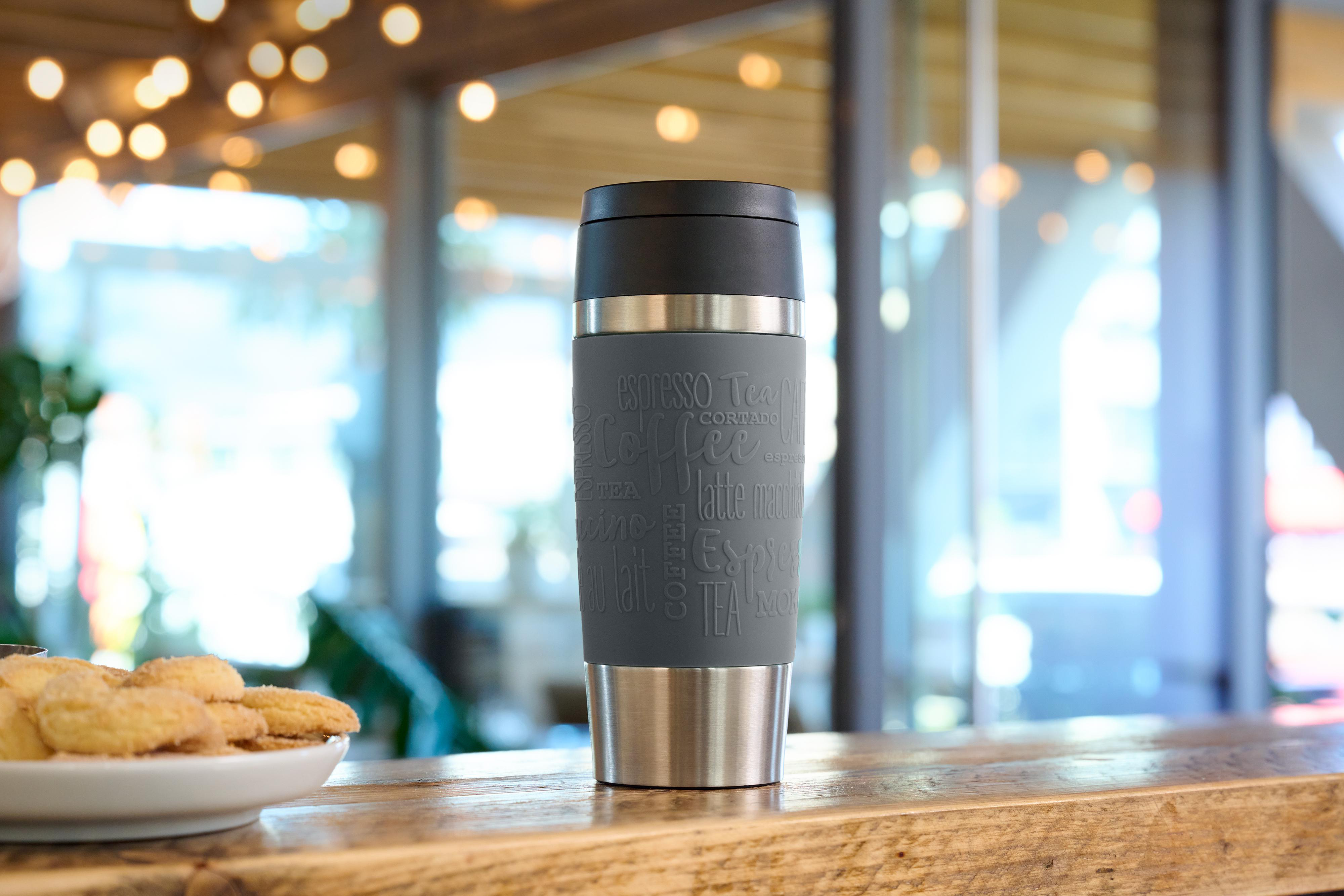 Ein grauer Reisebecher mit kaffeebezogenem Text auf einer Theke.