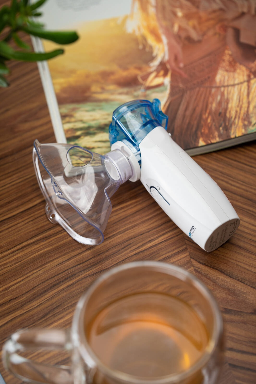 Biało-niebieski nebulizator medyczny leży na drewnianym stole obok czasopisma i szklanki herbaty.
