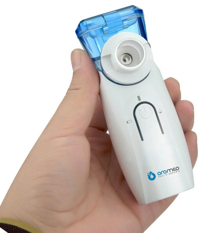 Ręka trzyma biało-niebieski nebulizator medyczny. Nebulizator ma przycisk zasilania i logo z napisem 'oromed'.