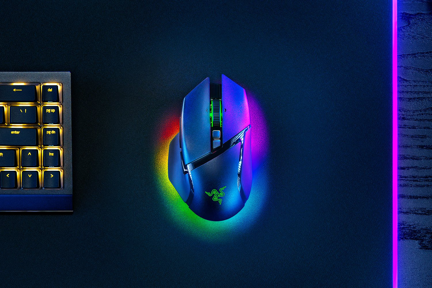 Un mouse da gioco su un tappetino per mouse. Una tastiera sullo sfondo. Il mouse ha l'illuminazione RGB.