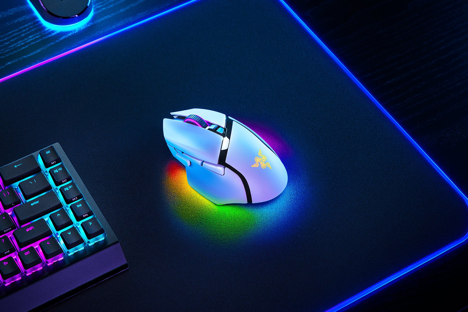 Mouse da gioco bianco su un tappetino nero con luci colorate. Tastiera sullo sfondo.