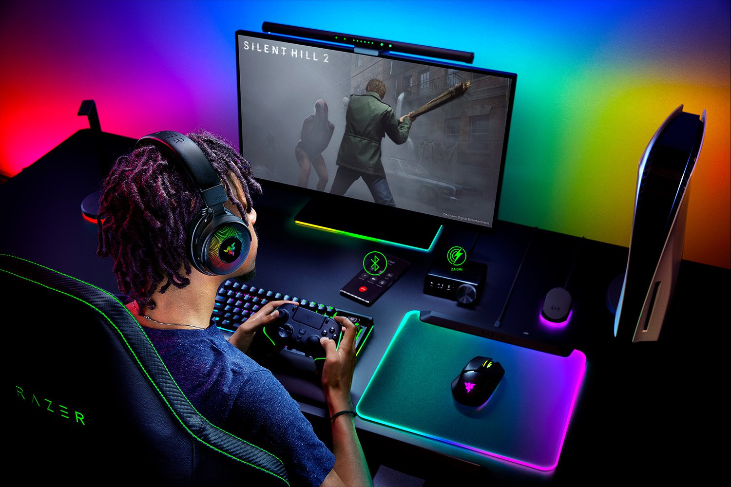 Person spielt mit Kopfhörern, Controller und Tastatur. Ein Bildschirm zeigt ein Spiel. Rechts ist eine PS5.