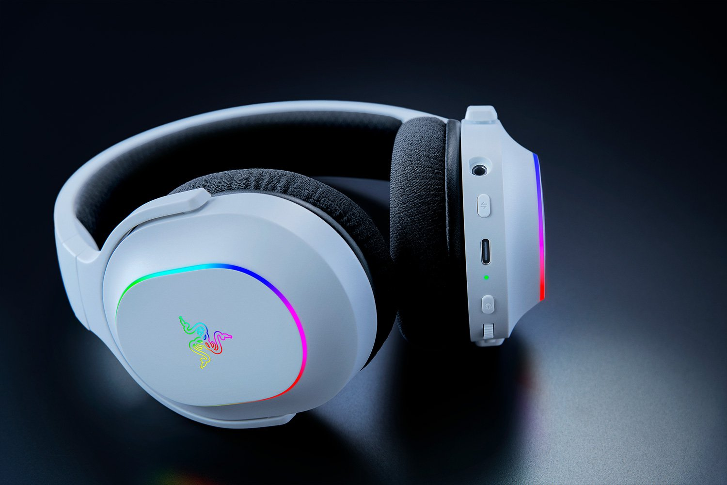 Weiße Gaming-Kopfhörer mit RGB-Beleuchtung auf den Ohrmuscheln und einem Razer-Logo, auf dunkler Oberfläche.