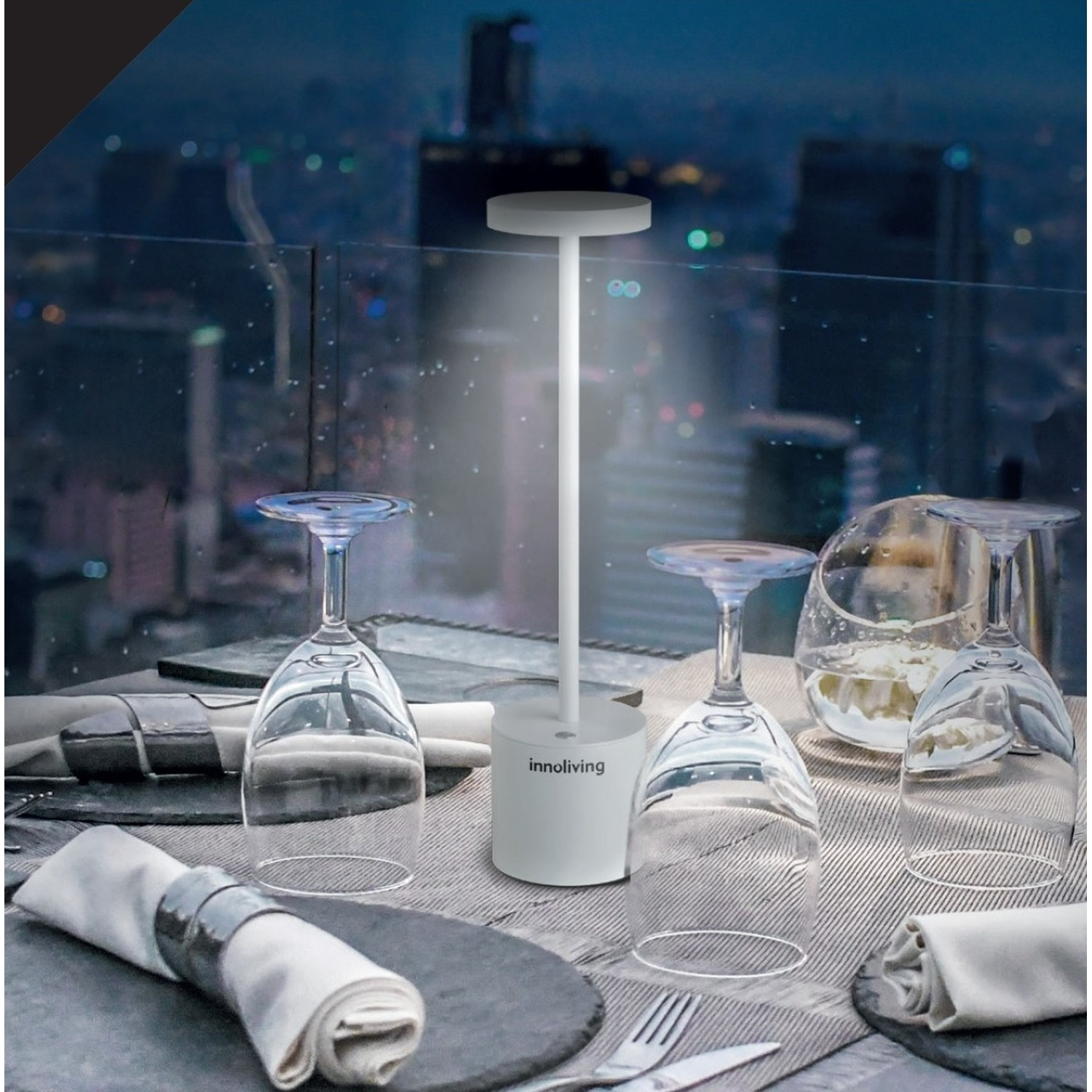 Una lampada da tavolo bianca illumina calici, un'apparecchiatura con skyline sullo sfondo.