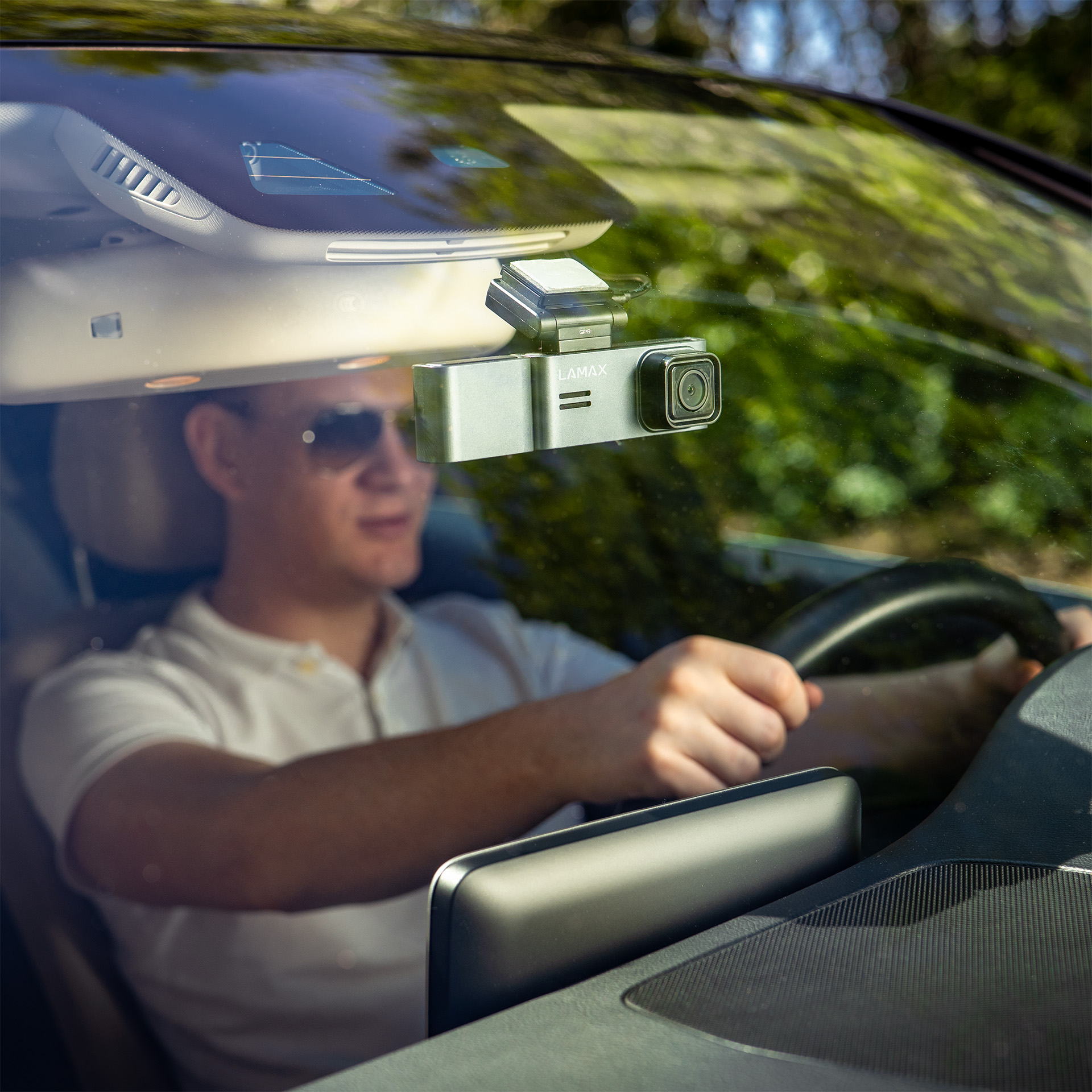 Férfi autót vezet dashcam-mel. Férfi napszemüvegben, dashcam a szélvédőn, homályos háttér.