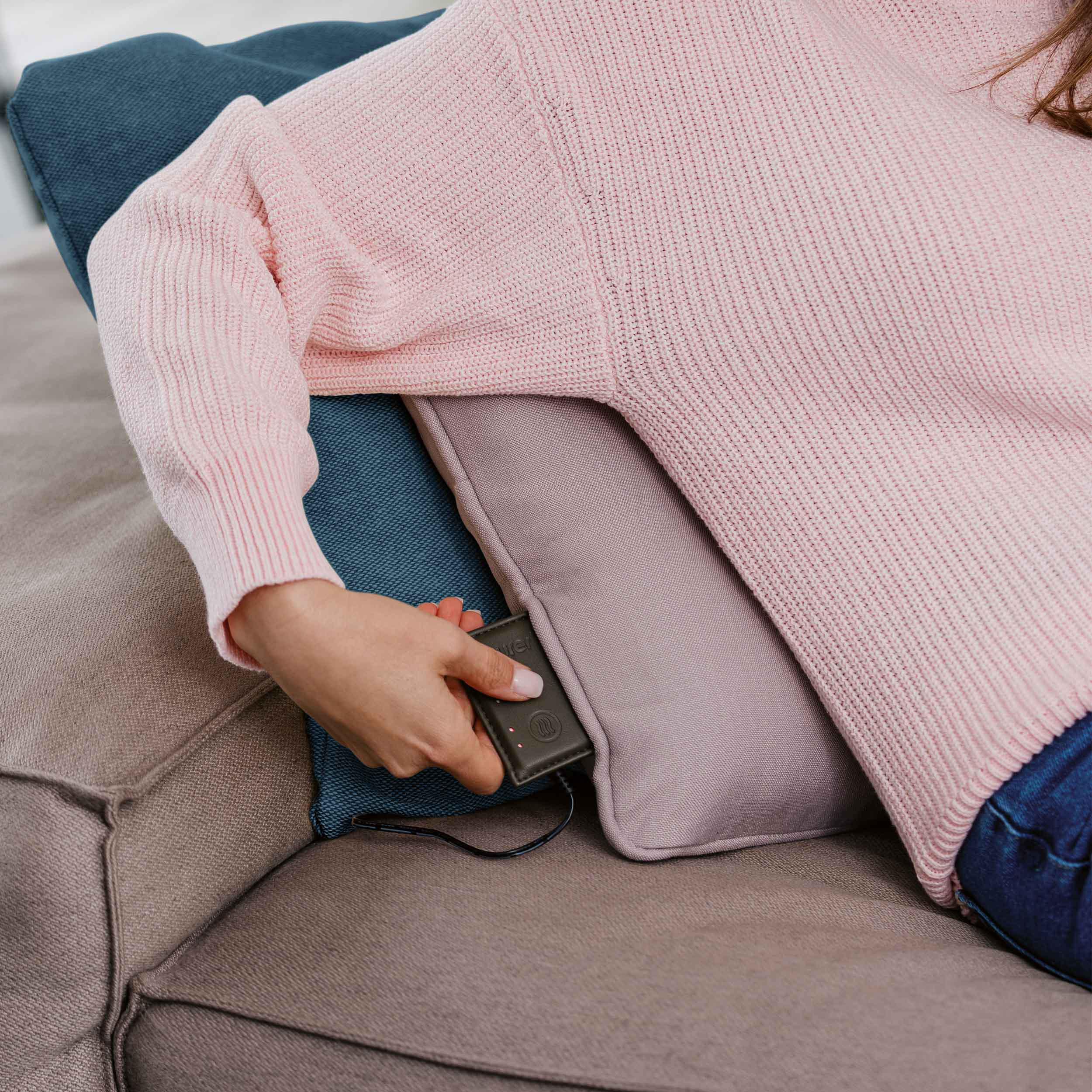 Die Hand einer Person, die ein Steuergerät auf einem Sofa mit Kissen hält.
