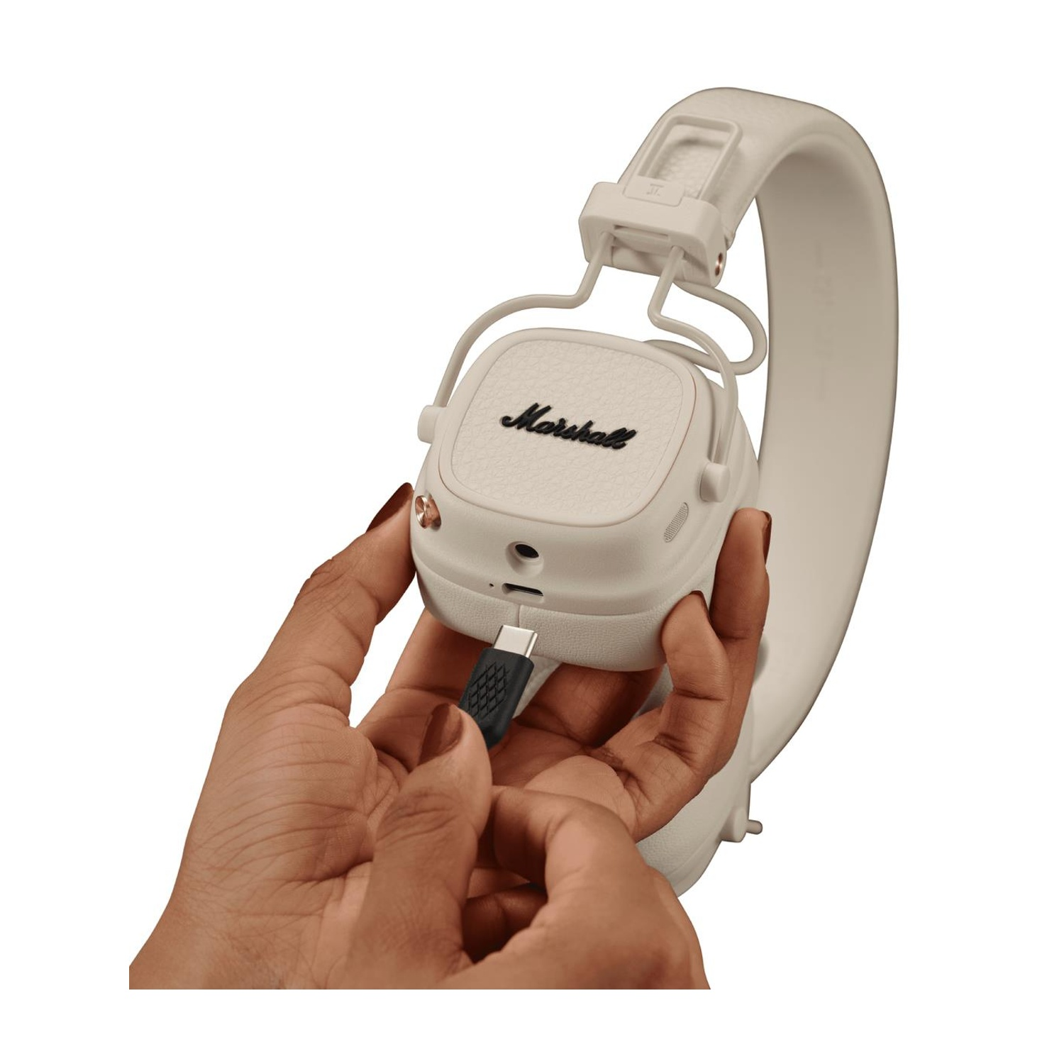 Una persona tiene in mano delle cuffie Marshall bianche, inserendo un cavo USB-C nella porta.
