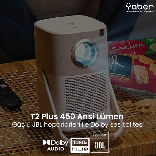 'T2 Plus' ve 'JBL' metinli bej ve beyaz bir projektör. Ahşap bir yüzeyde duruyor.