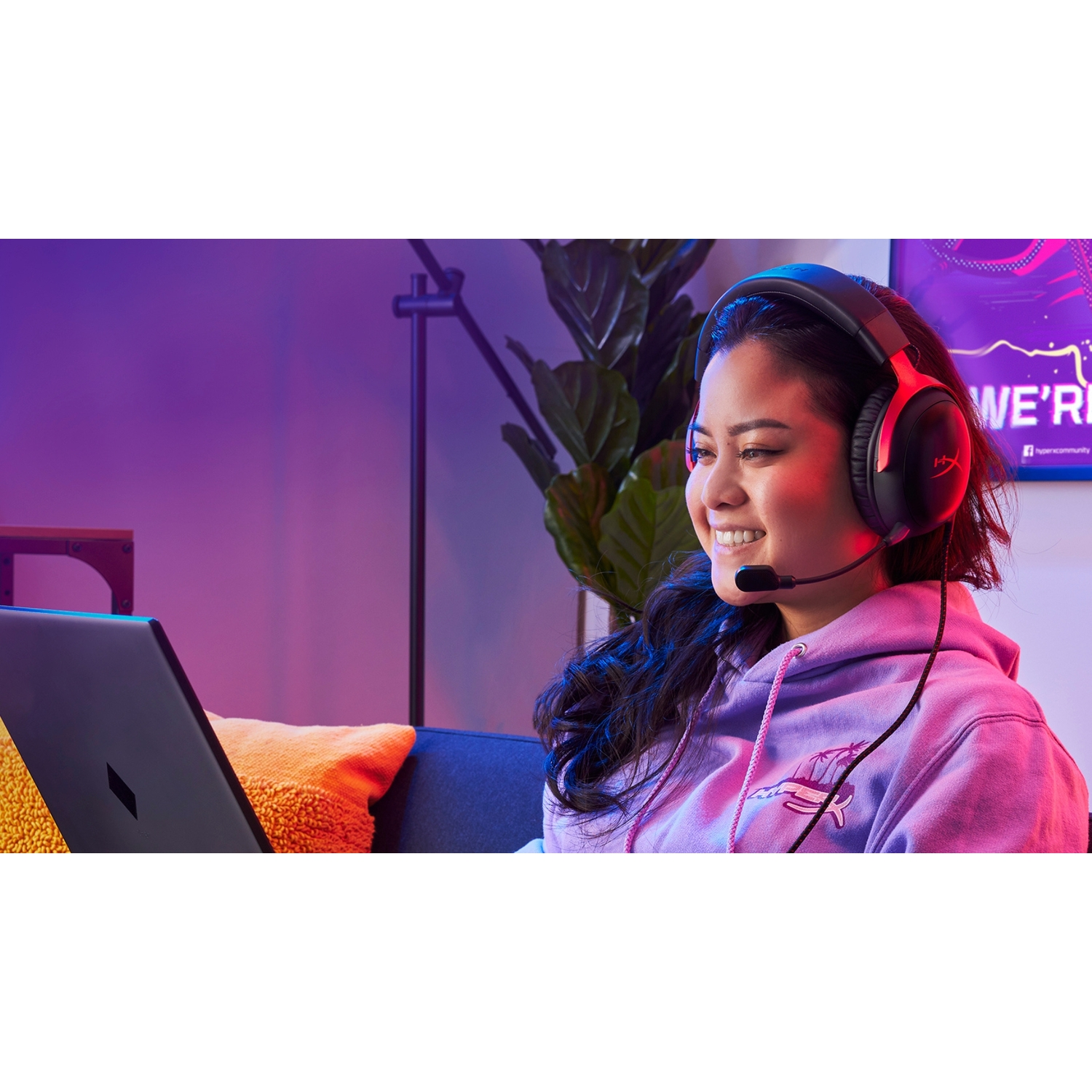 Vrouw met headset, glimlachend, zittend voor een laptop met een paarse achtergrond.