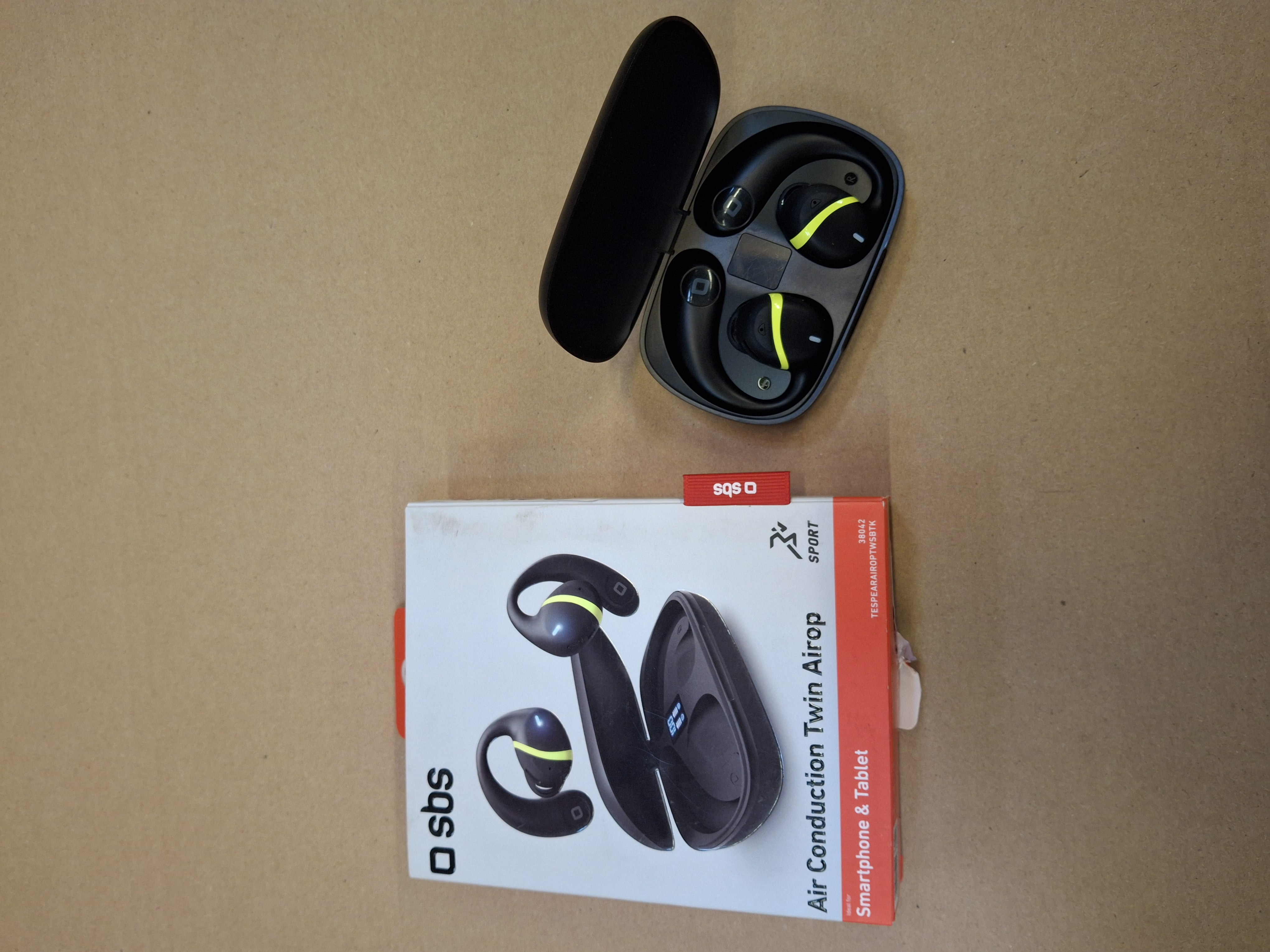 Czarne słuchawki z żółtymi akcentami w czarnym etui ładującym i na opakowaniu.