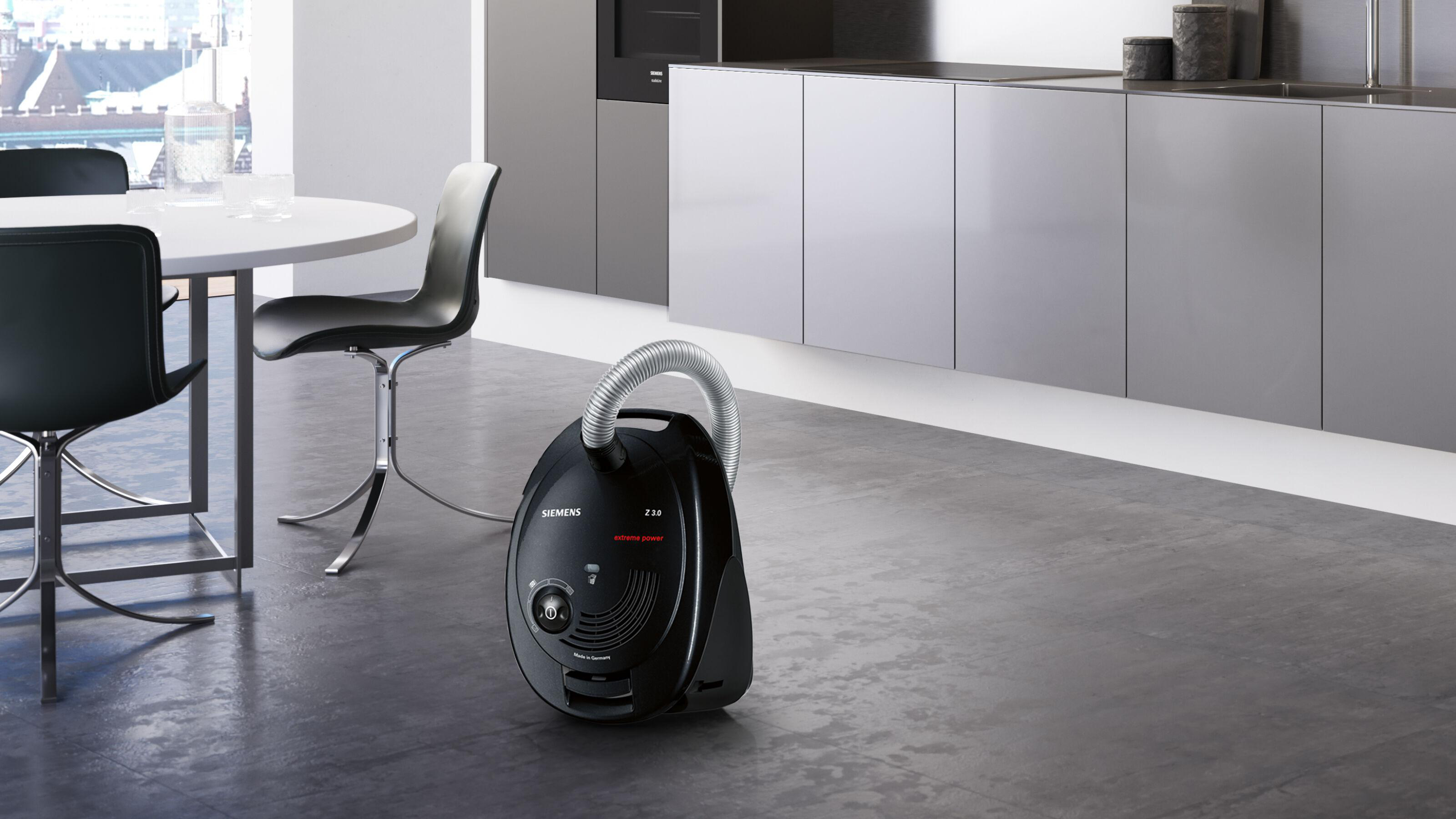 Schwarzer Staubsauger in moderner Küche. Tisch und Stühle im Hintergrund.