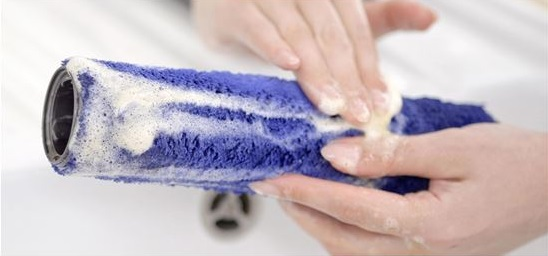 Dłonie czyszczą niebieską, cylindryczną szczotkę z pianą w białym zlewie. Skupienie na czyszczeniu.