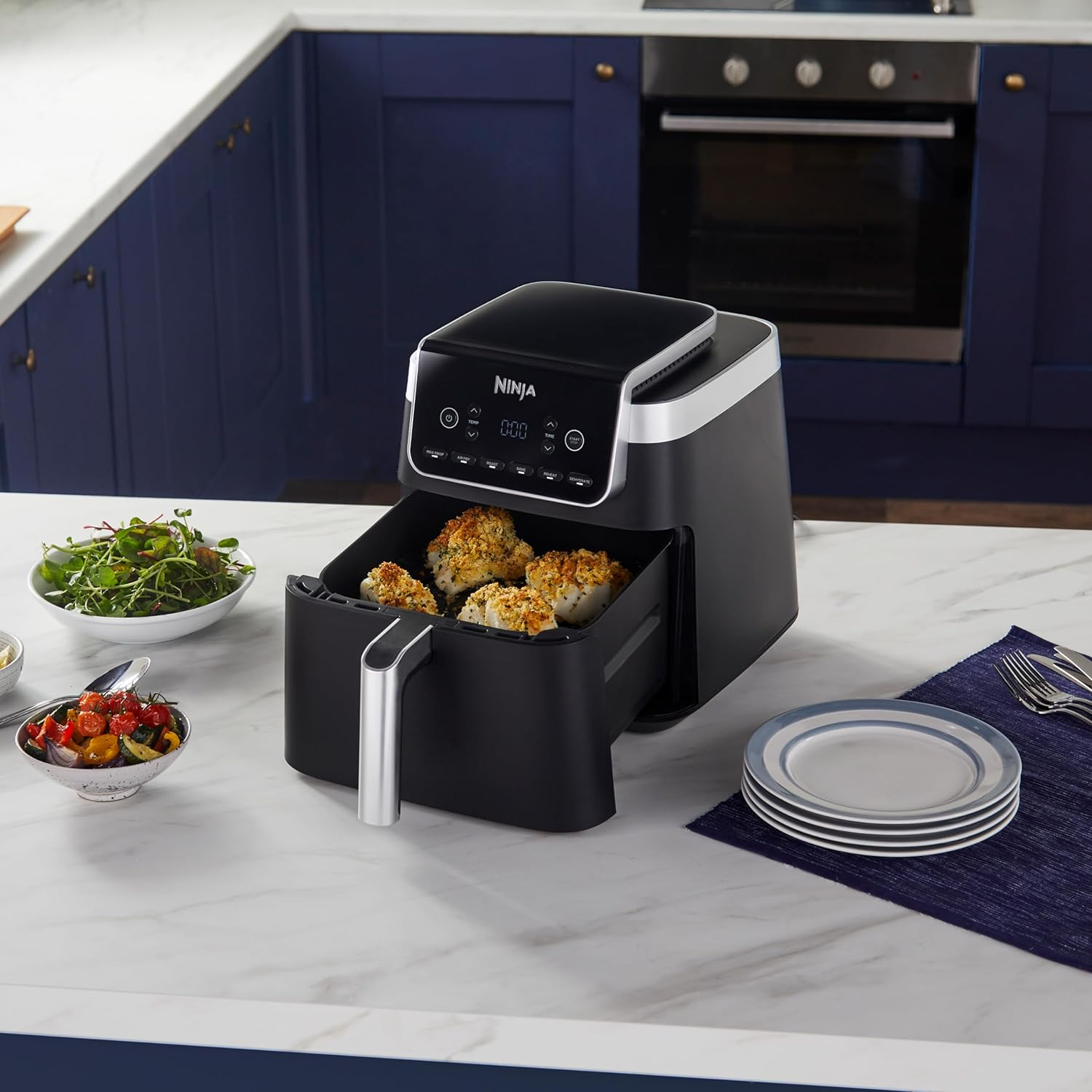 Friggitrice ad aria nera con cibo all'interno. Altri piatti e piatti sono sul bancone in cucina.