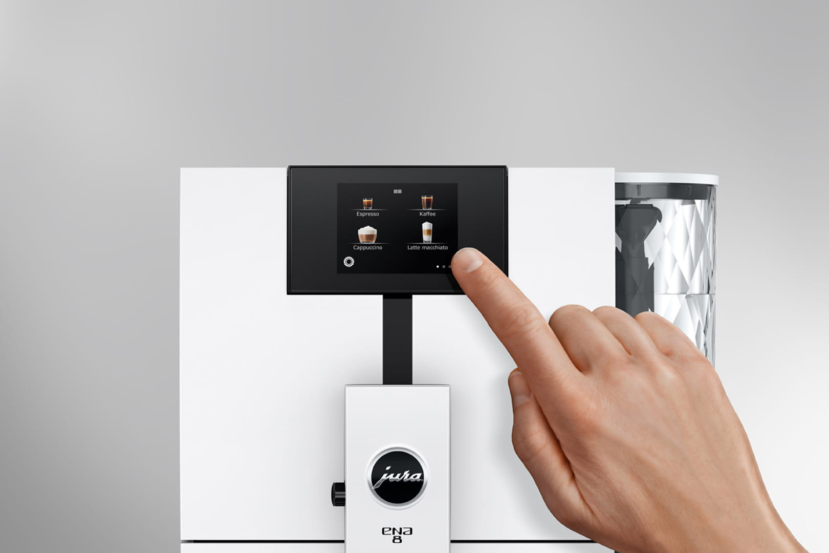 Una mano tocca il touchscreen di una macchina da caffè bianca Jura ENA 8. Lo schermo mostra le opzioni caffè.