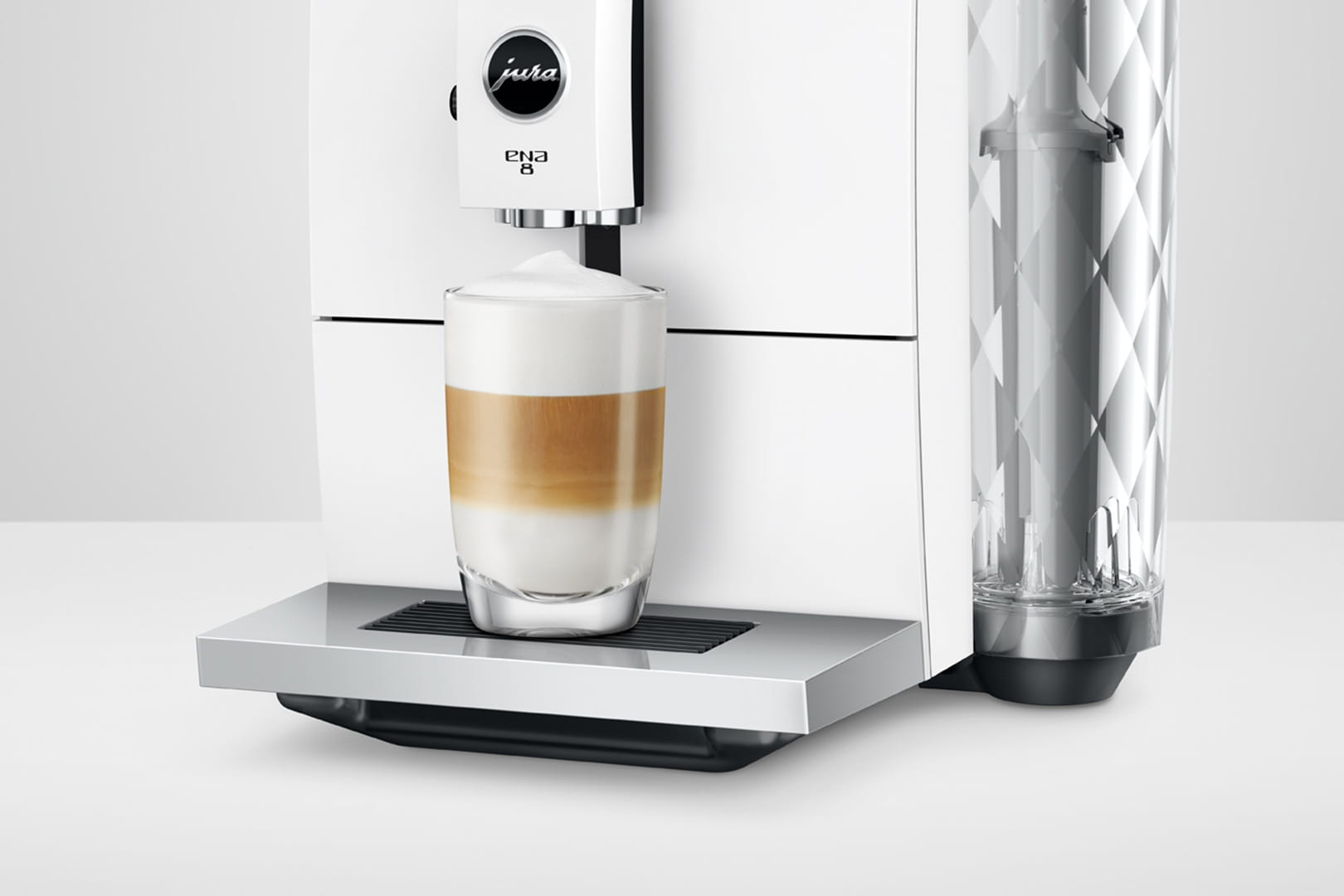 Una macchina da caffè Jura Ena 8 bianca con un bicchiere di latte macchiato a strati e un contenitore per l'acqua.