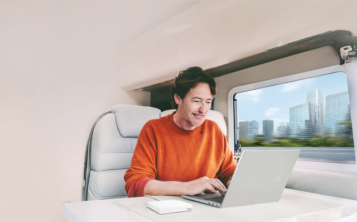 Un homme en pull orange utilise un ordinateur portable dans un véhicule avec vue sur la ville.