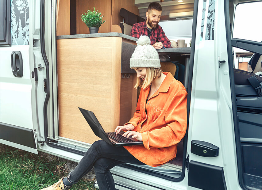 Un couple dans un camping-car, l'un travaillant sur un ordinateur portable, l'autre à table.