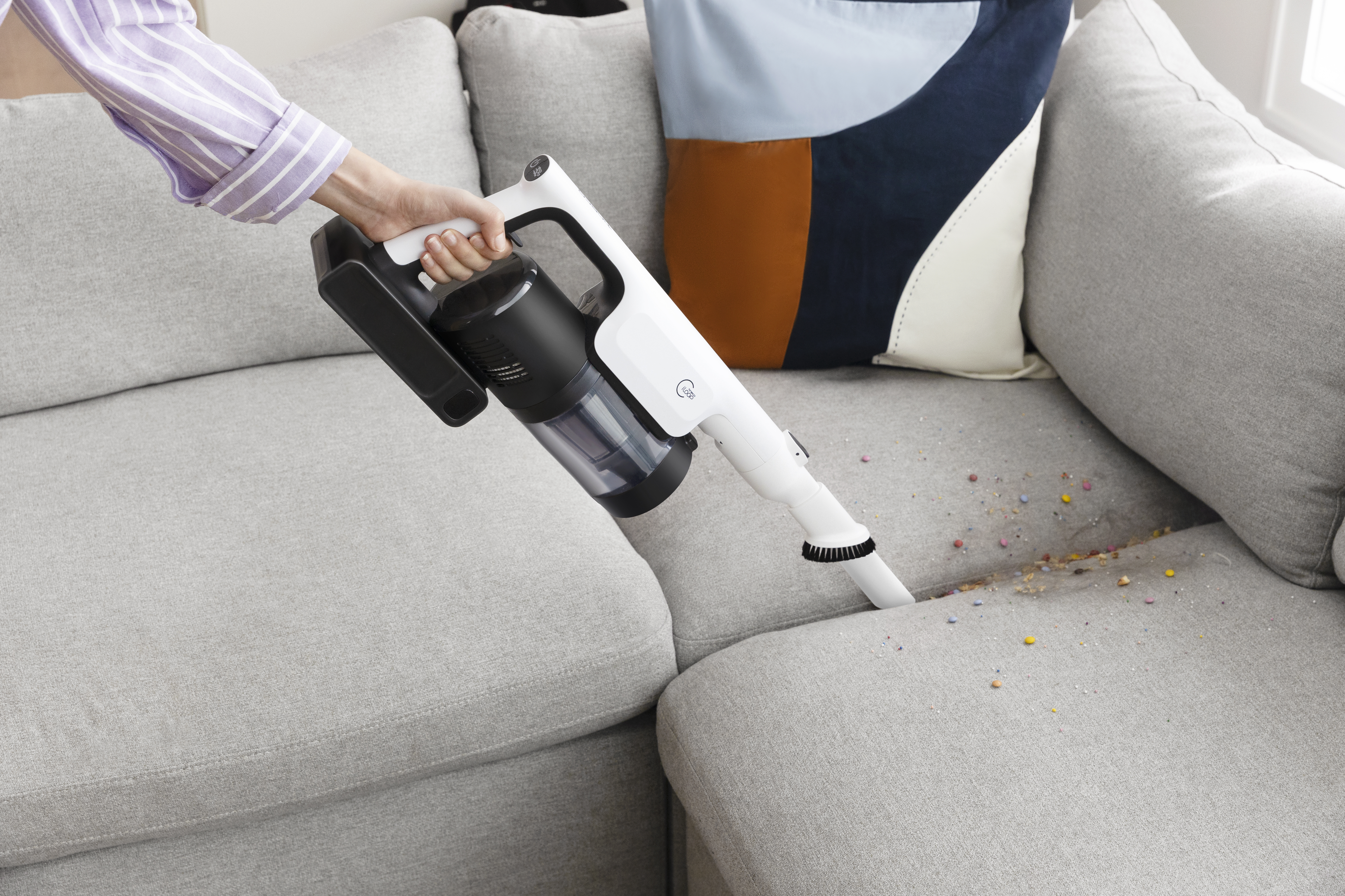 Eine Person, die ein graues Sofa absaugt. Der Staubsauger ist weiß.