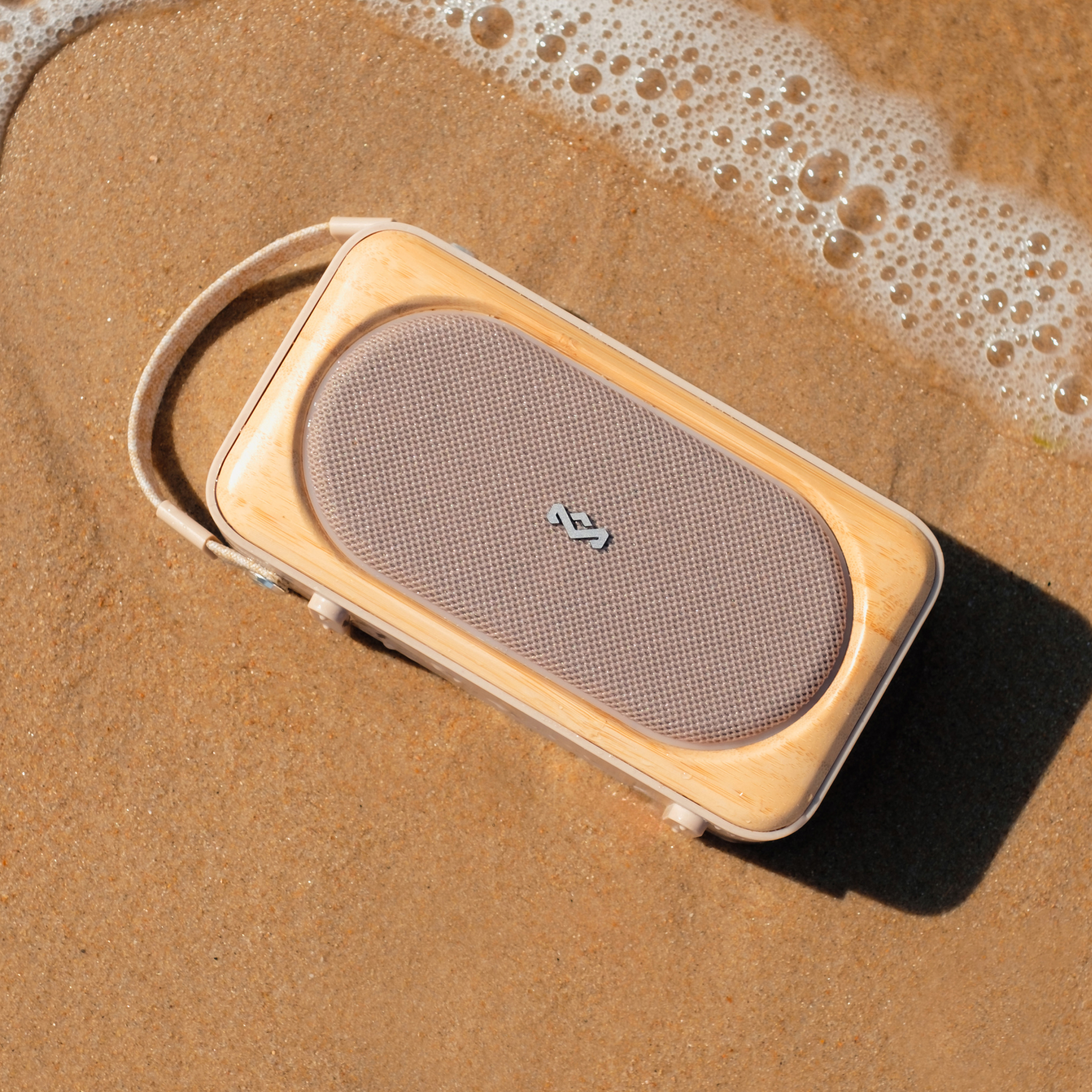 Ein hölzerner Lautsprecher an einem Sandstrand mit Wasser im Hintergrund, an einem sonnigen Tag.