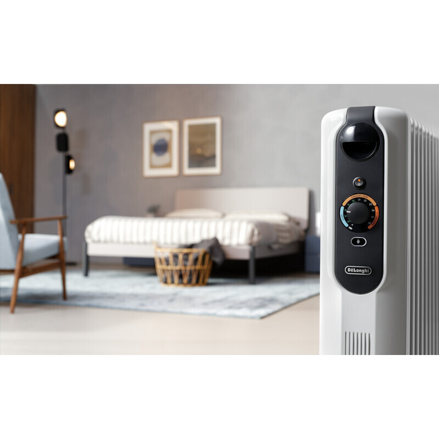 Witte DeLonghi oliegevulde radiator met bedieningspaneel. Achtergrond slaapkamer.