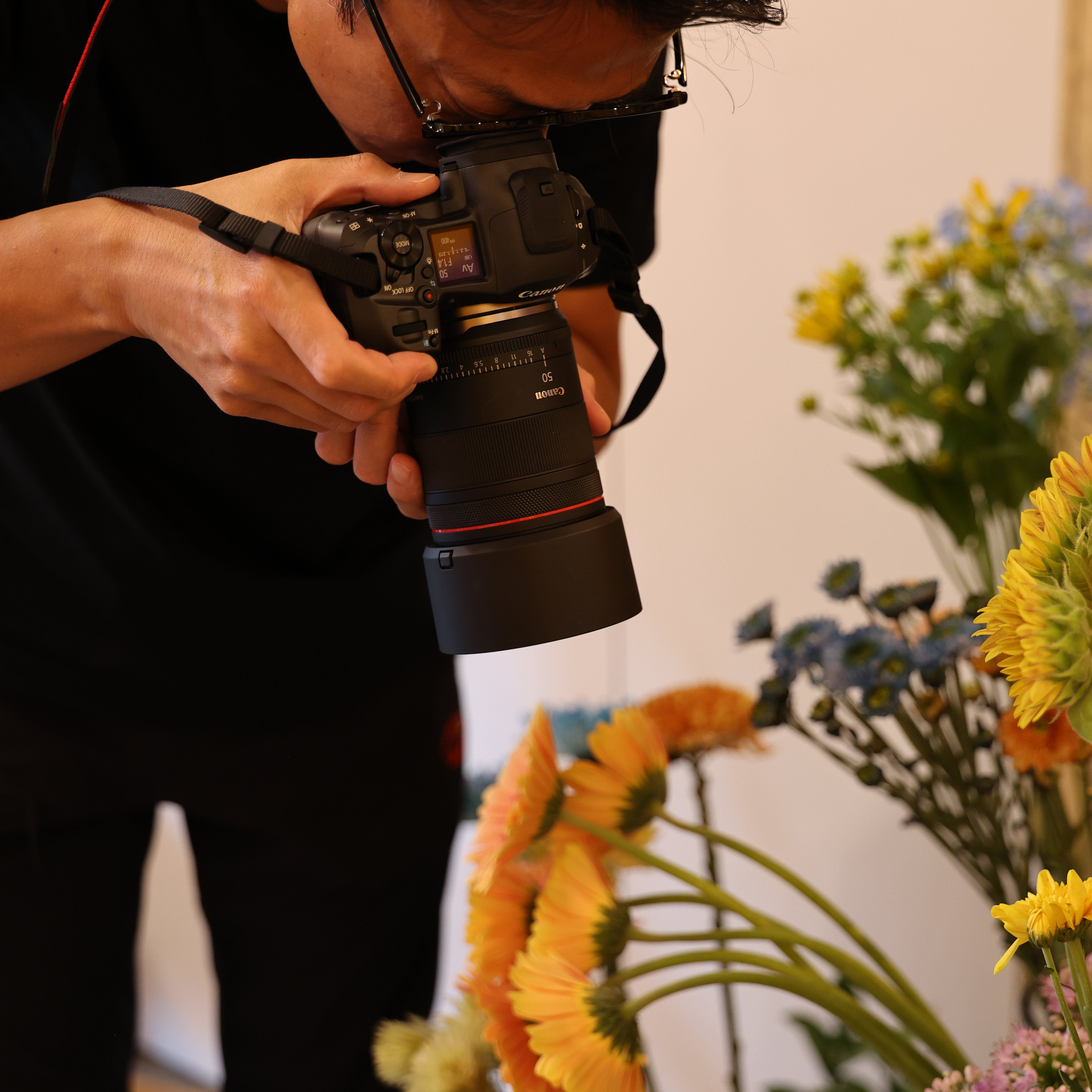 Photographe prenant une photo de fleurs orange et bleues avec un appareil photo Canon.