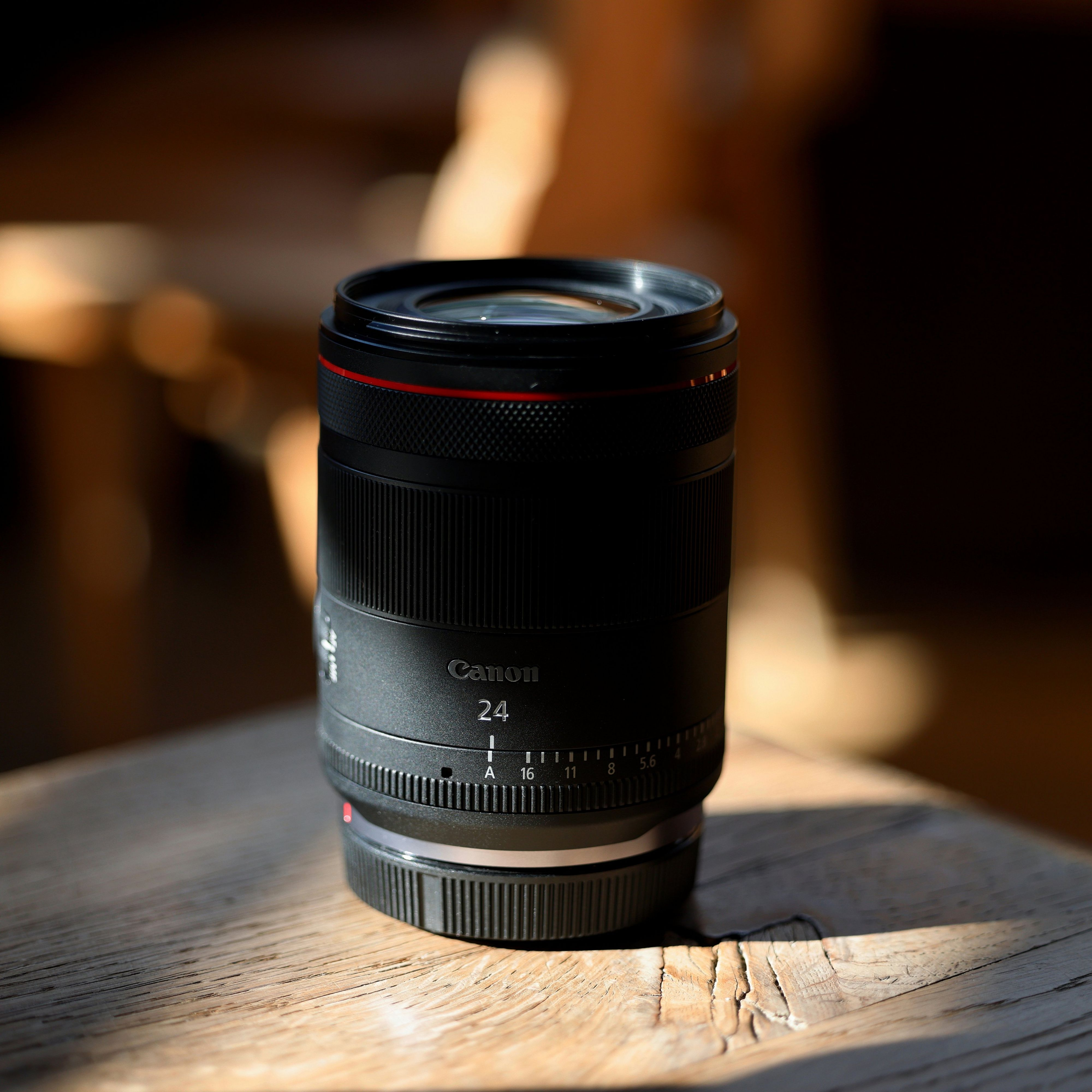Un objectif d'appareil photo Canon noir est posé sur une surface en bois. L'objectif est net et l'arrière-plan flou.