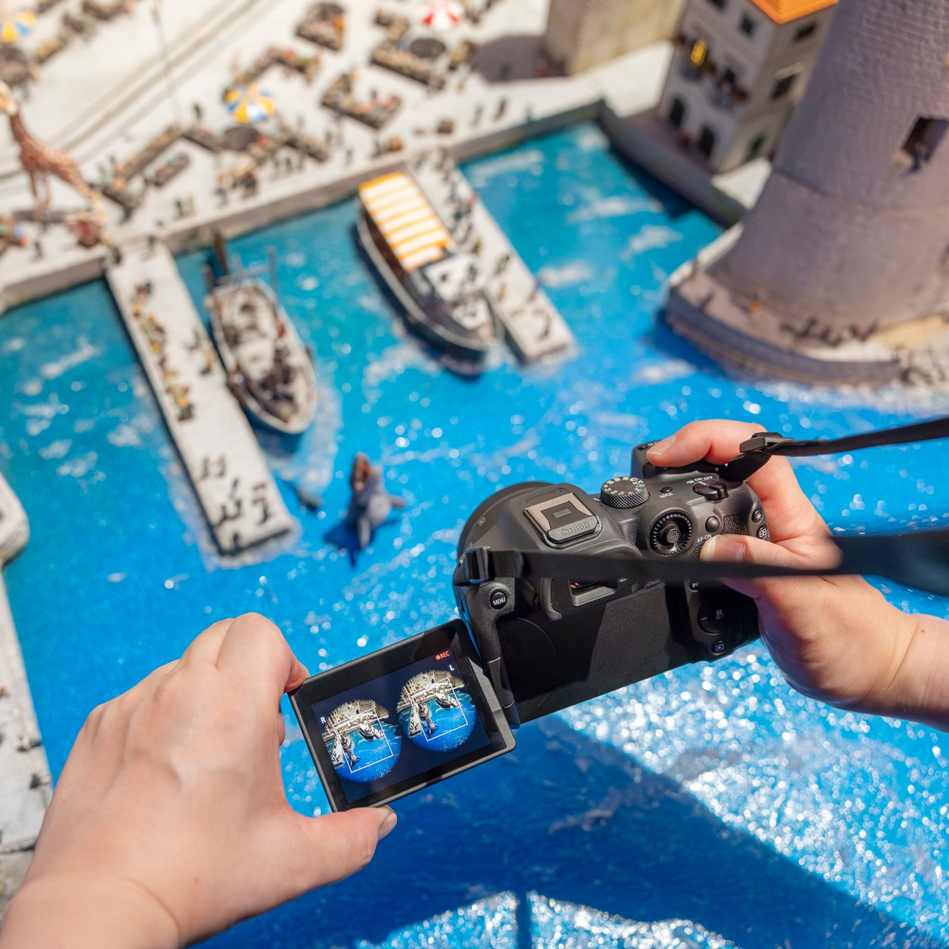 Une personne tient un appareil photo, regardant l'écran montrant une ville miniature avec de l'eau et des bateaux.
