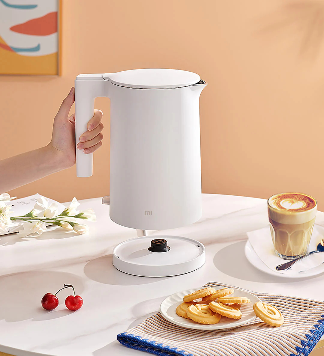 Biały czajnik elektryczny trzymany przez dłoń i filiżanka kawy.