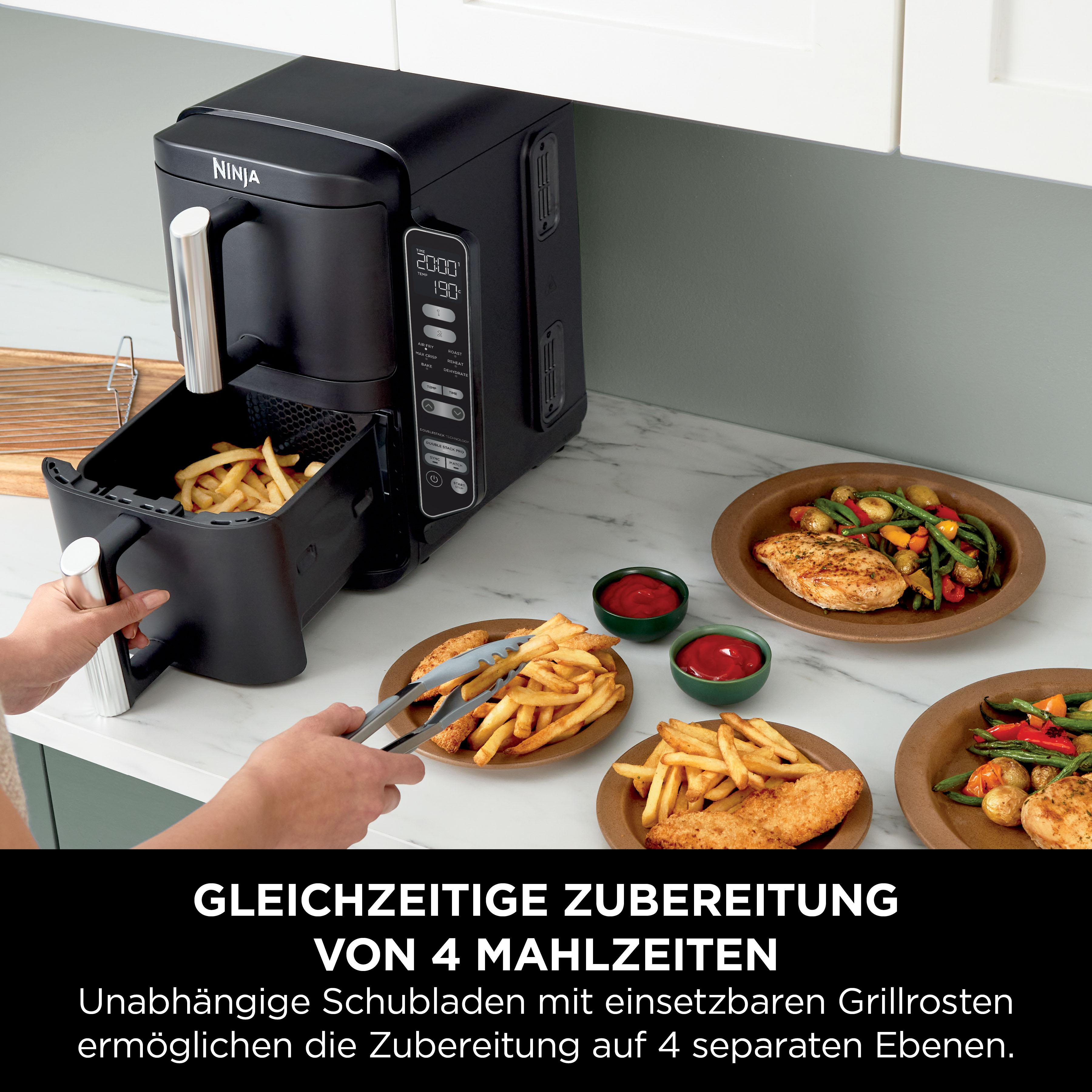 Schwarze Ninja-Heißluftfritteuse mit Pommes und Hähnchen auf Tellern. Eine Person benutzt eine Zange.
