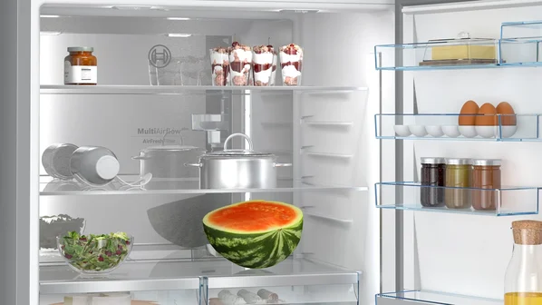 Çeşitli yiyeceklerin bulunduğu buzdolabı içi. Yarım karpuz, salata ve raflarda kavanozlar var.